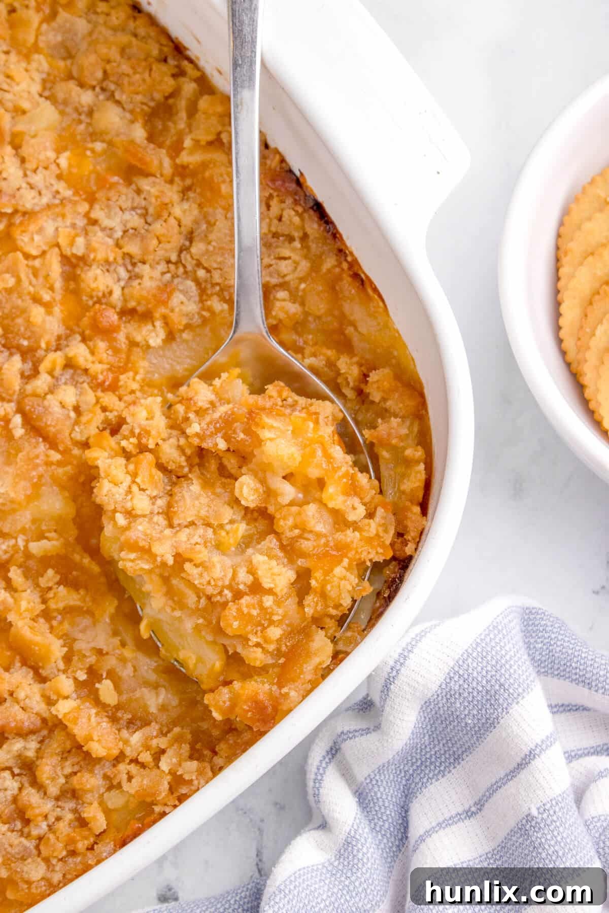 Pineapple casserole in a pan with a serving spoon, showcasing its golden, bubbly crust and warm, cheesy pineapple interior.