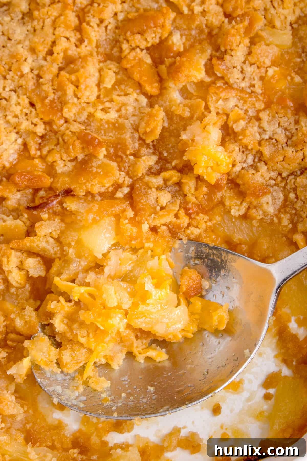 A serving spoon embedded in a pan of pineapple casserole, highlighting its appealing golden-brown, crispy topping.