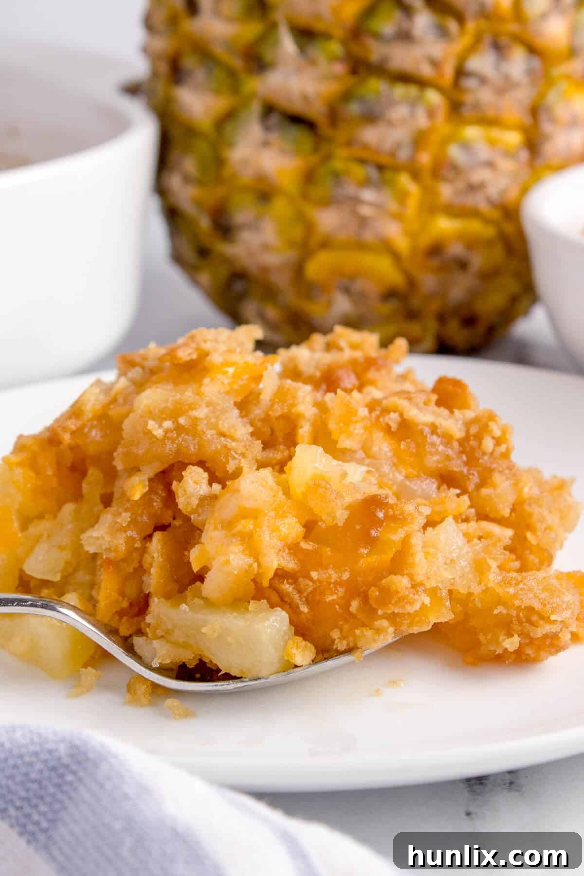 A scoop of golden-brown pineapple casserole served on a white plate, ready to be savored.