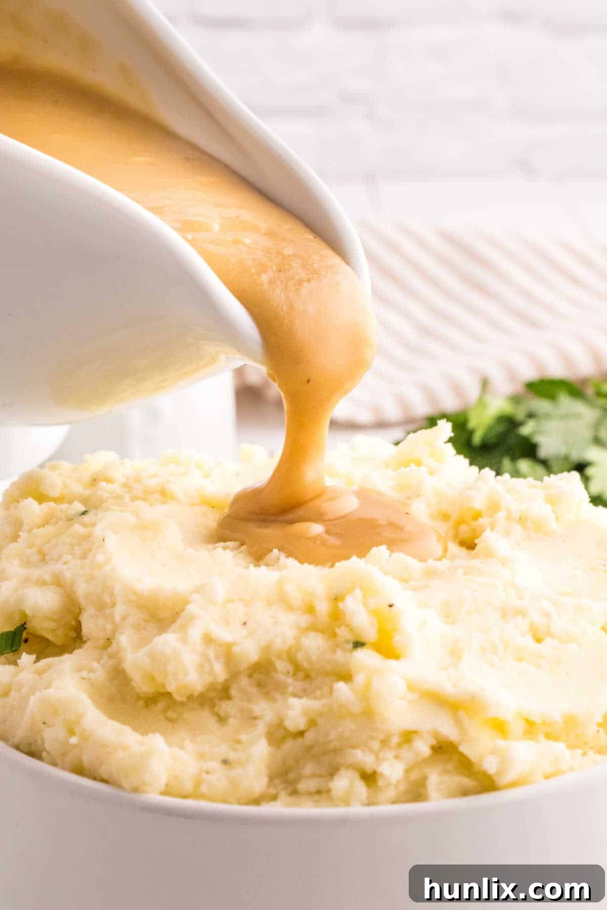 A stream of rich, brown gravy being poured from a gravy boat over a generous serving of creamy mashed potatoes.