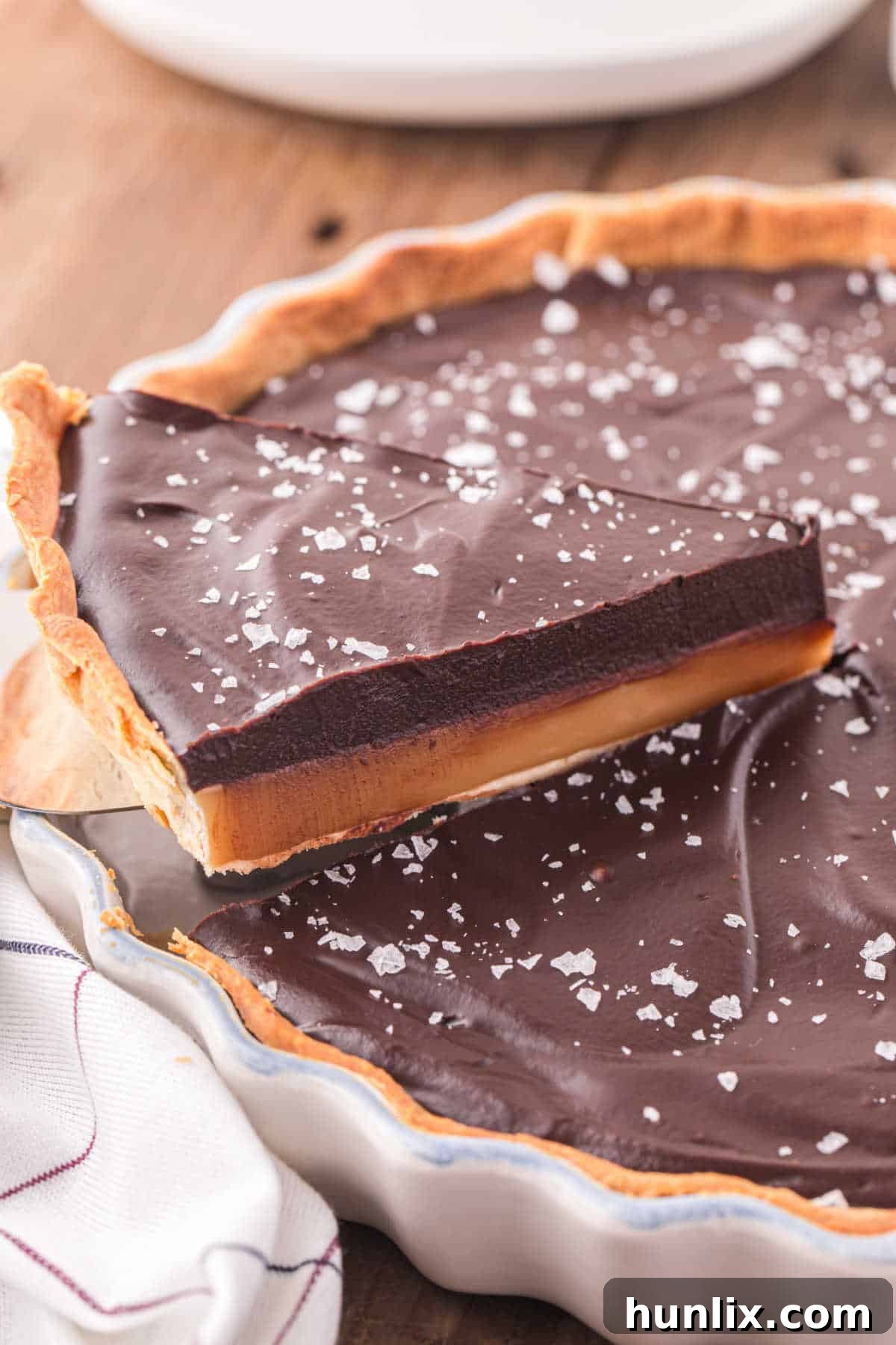 A beautifully presented slice of chocolate caramel tart on a spatula, showcasing its distinct layers.