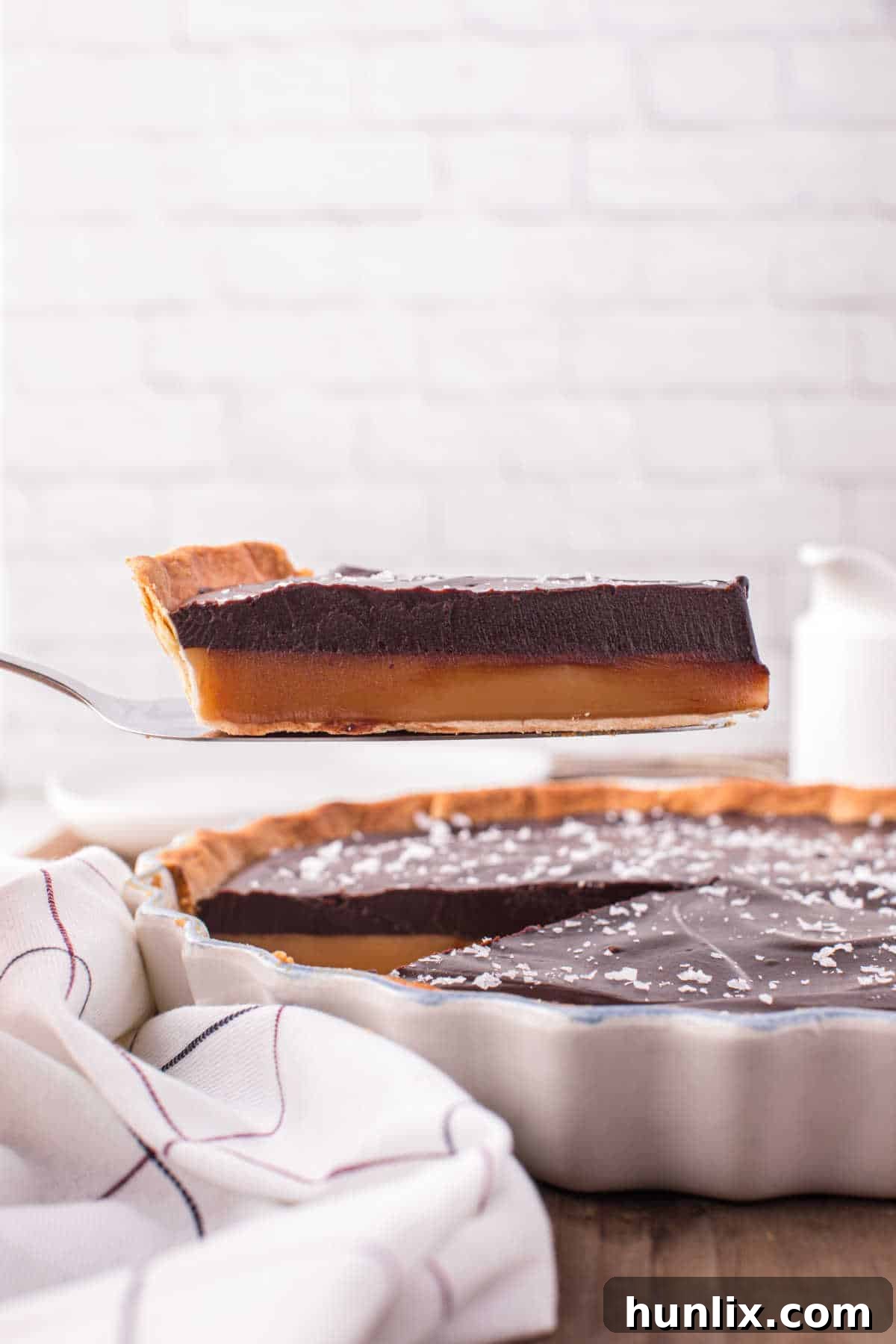 A second close-up view of a slice of chocolate caramel tart on a spatula, highlighting its glossy surface and layers.