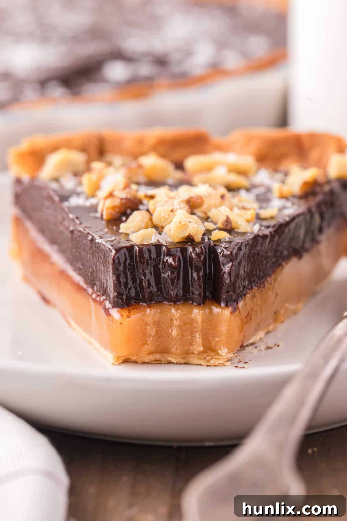 A slice of chocolate caramel tart with a corner missing, showing a bite taken out, inviting viewers to taste.