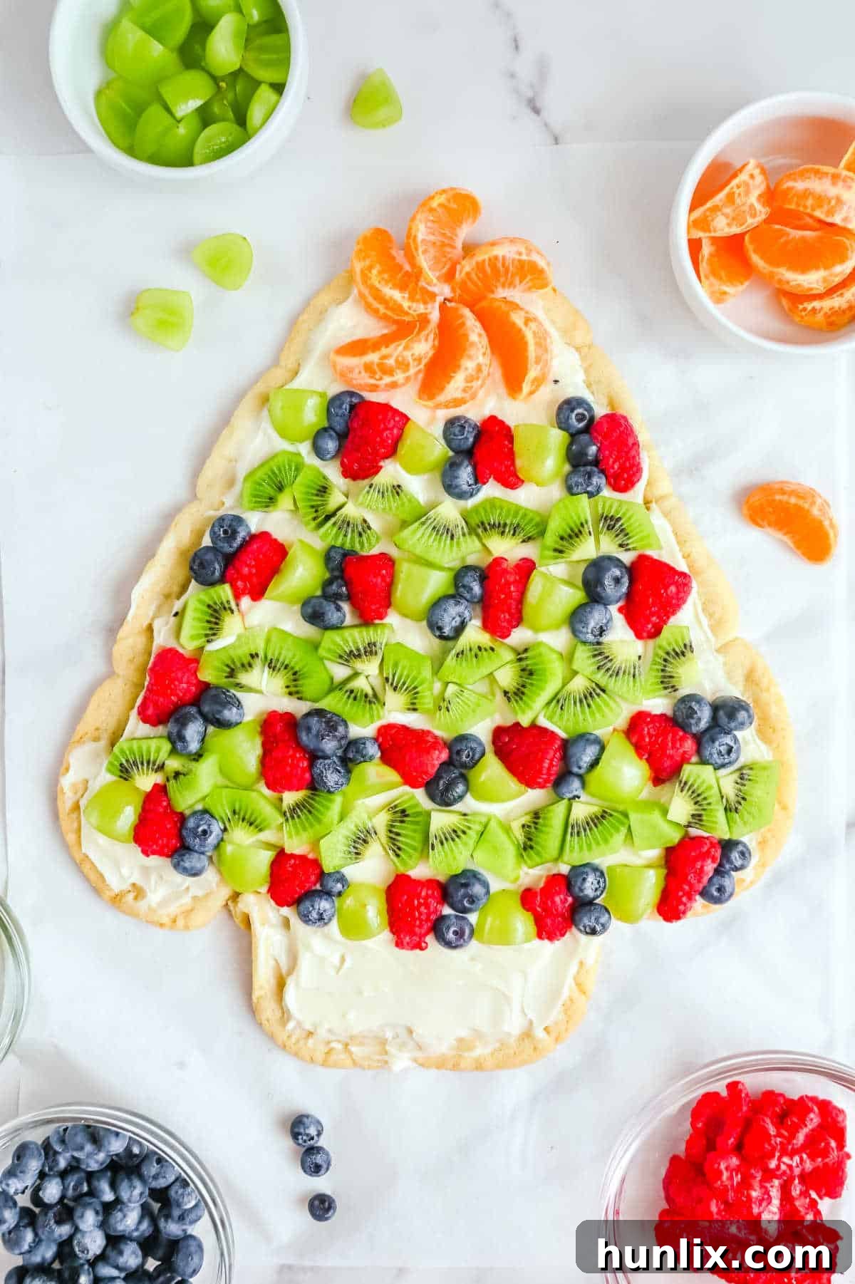 A beautifully decorated Sugar Cookie Christmas Tree with fresh fruit and cream cheese frosting on a white surface, ready for holiday celebrations.