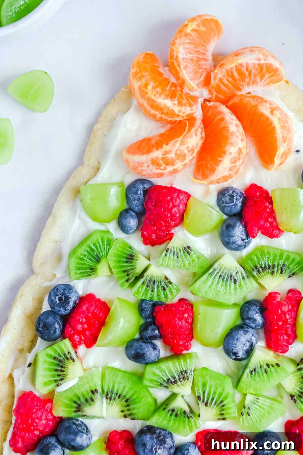 A sugar cookie Christmas tree on a white surface, showcasing its vibrant fruit decorations.