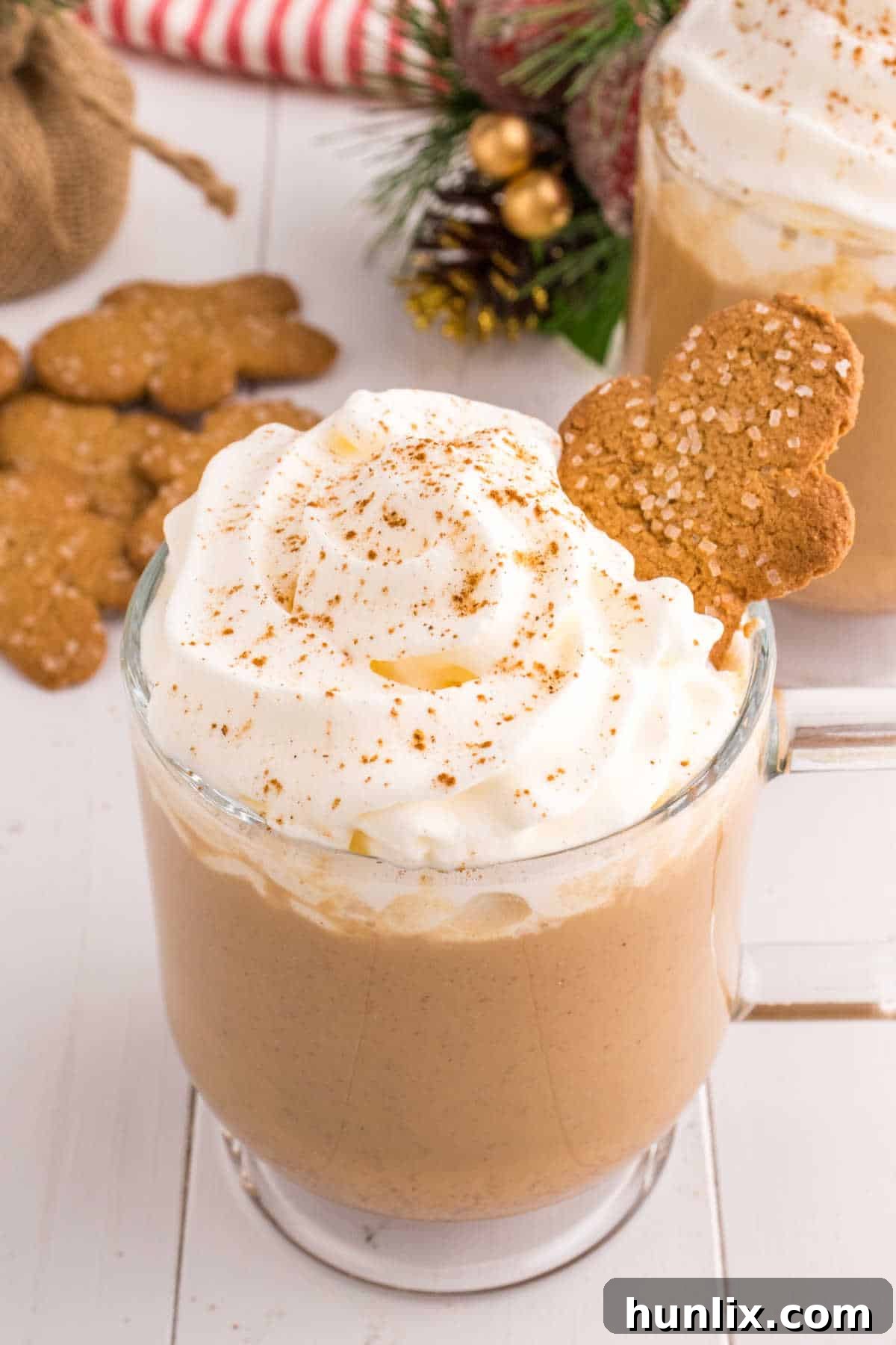 Yuletide Gingerbread Eggnog 2 A glass mug filled with creamy gingerbread eggnog, garnished with whipped cream and a gingerbread cookie, set against a festive holiday background.