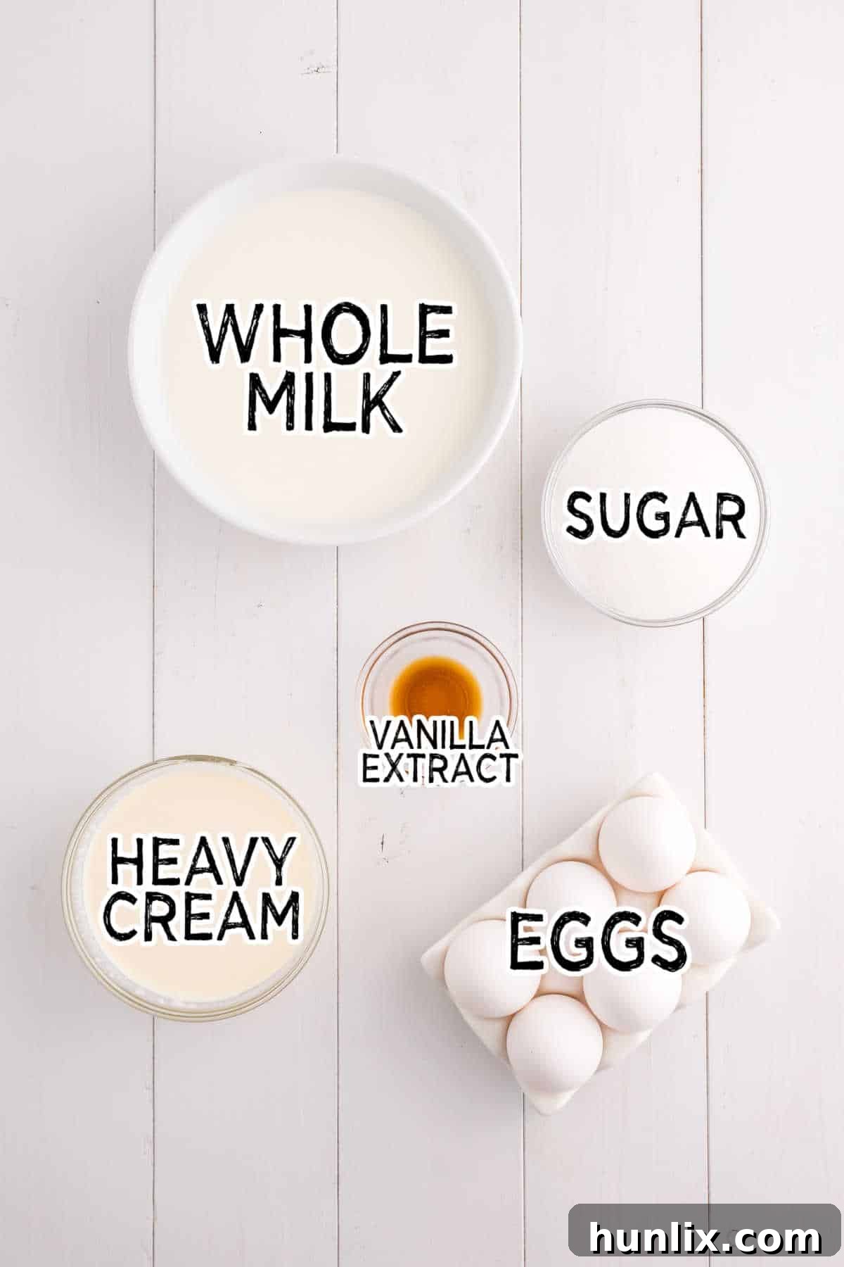 Yuletide Gingerbread Eggnog 3 A selection of ingredients for the eggnog base, including eggs, milk, cream, sugar, and vanilla extract, arranged on a rustic white wooden board.