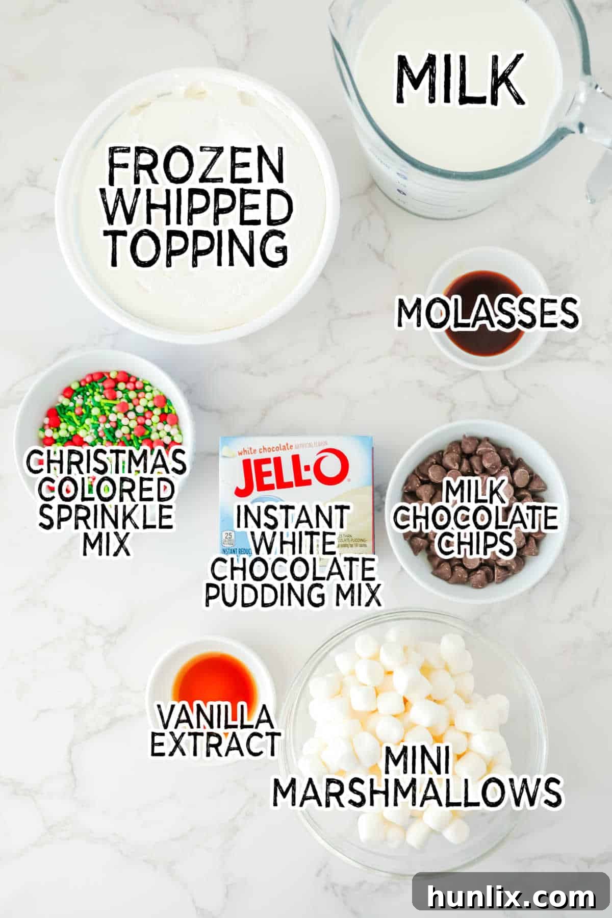 Ingredients for White Chocolate Elf Fluff, including whipped topping, pudding mix, milk, molasses, marshmallows, chocolate chips, and sprinkles.