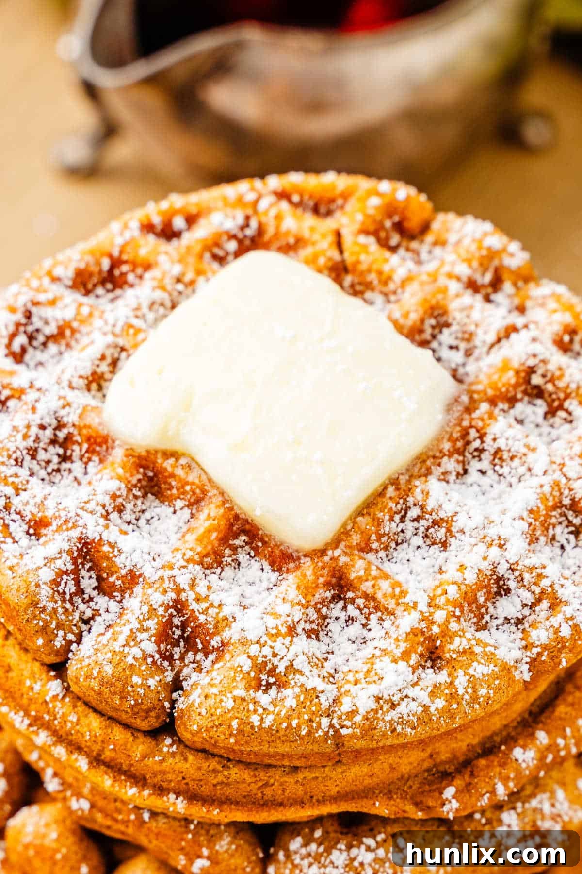 A plate of gingerbread waffles with butter and powdered sugar on top, ready to be served.
