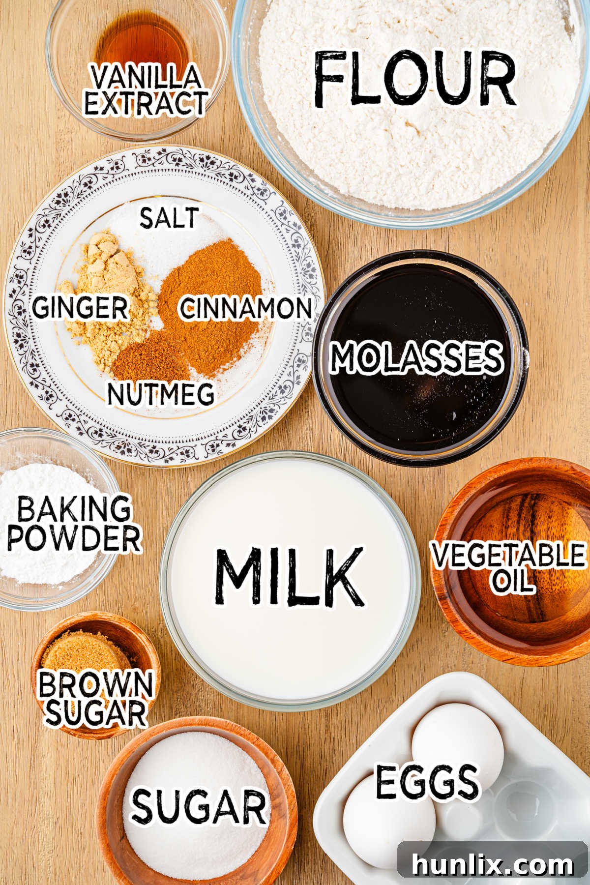 Ingredients laid out on a table to make gingerbread waffles, including flour, sugar, spices, eggs, milk, oil, molasses, and vanilla extract.