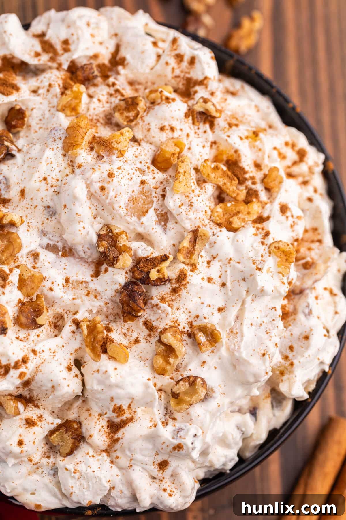 A serving of Apple Pie Fluff in a clear bowl, garnished with extra cinnamon and walnuts, highlighting its appealing layers.