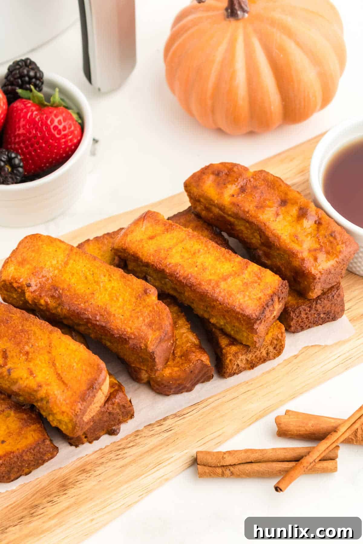 A generous pile of Air Fryer Pumpkin French Toast Sticks served on a wooden cutting board, ready for breakfast.