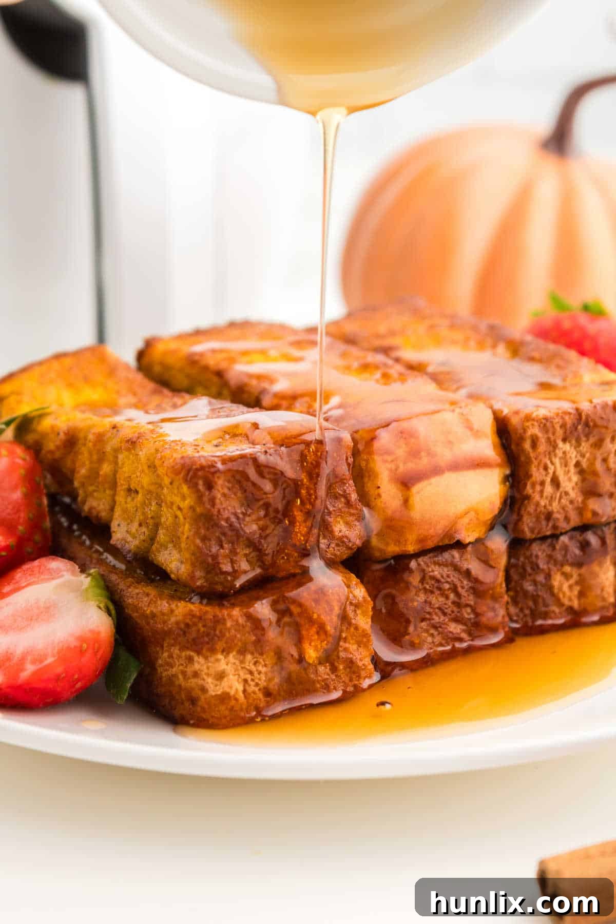 A close-up of Air Fryer Pumpkin French Toast Sticks piled high on a plate, with golden maple syrup drizzling over them.