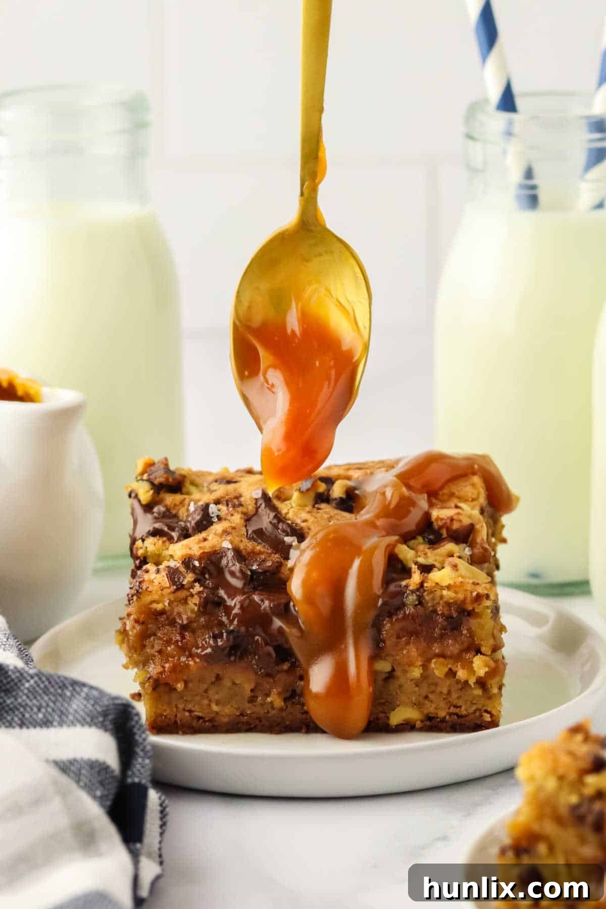 A close-up shot of a spoon drizzling luscious caramel sauce over a freshly baked piece of brown butter caramel blondie.