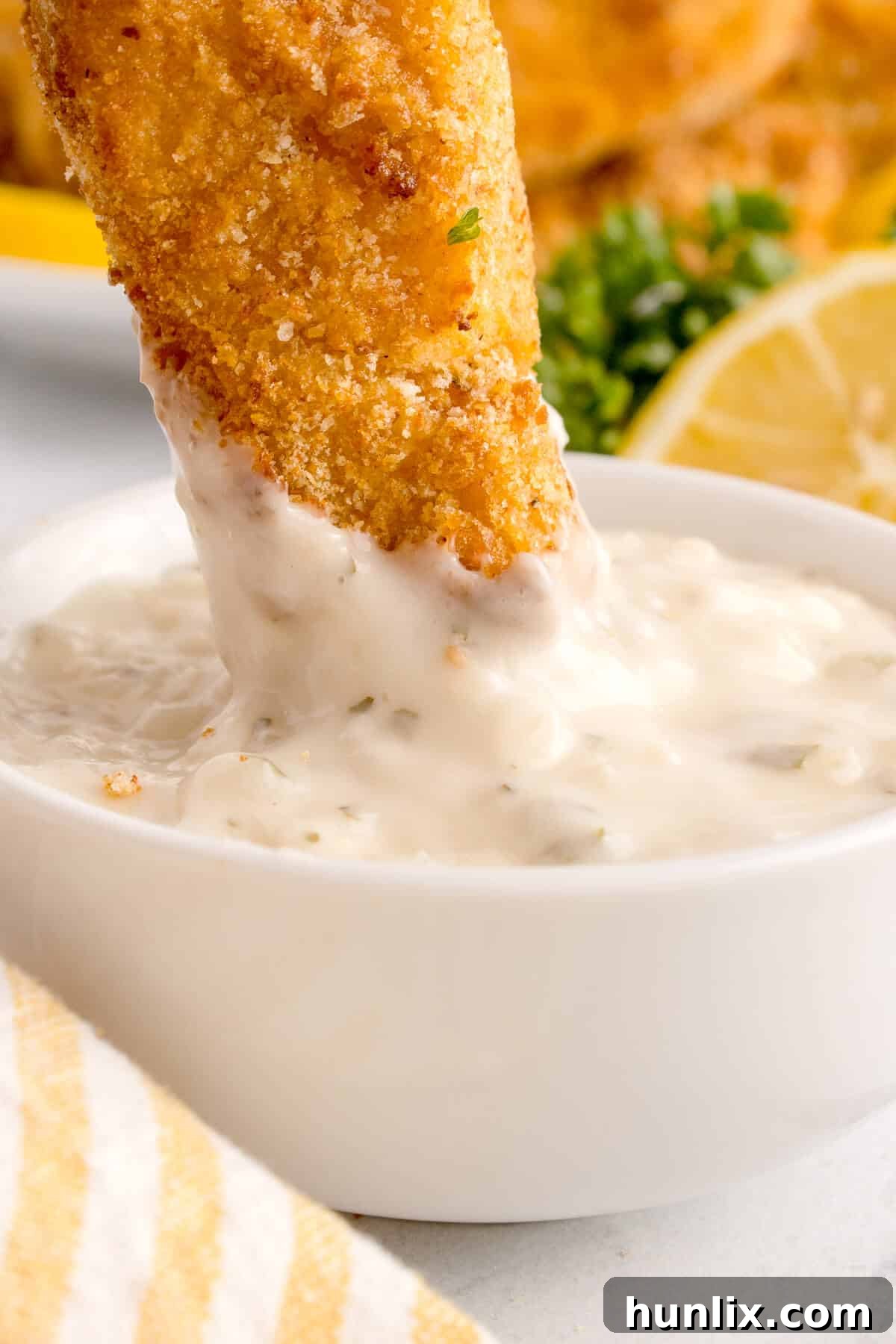 A crispy air-fried fish stick being dipped into tartar sauce.