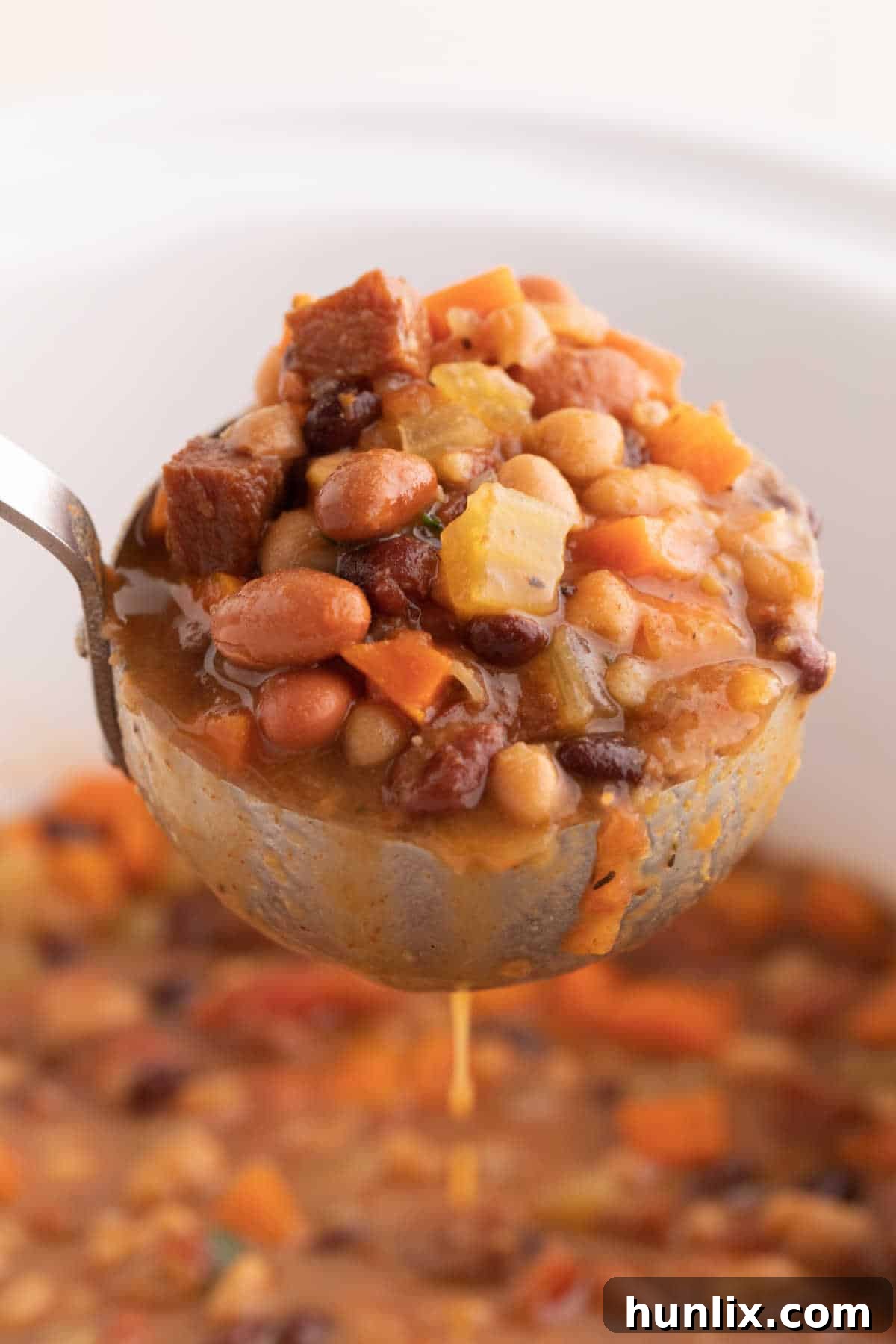 A ladle full of Crockpot Ham and Bean Soup, with soup in the background.