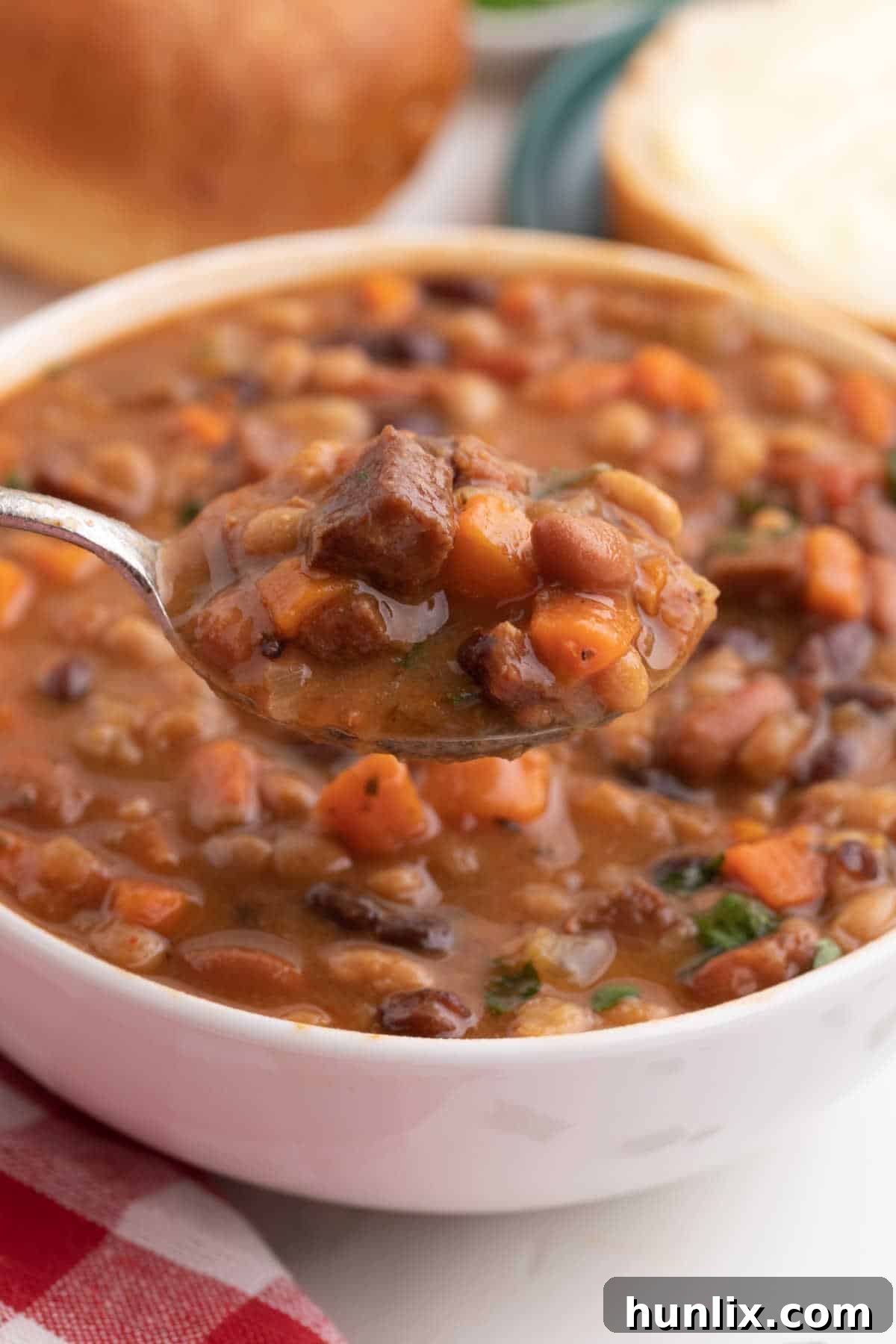 Ham and bean soup on a spoon held over a bowl, ready to eat.