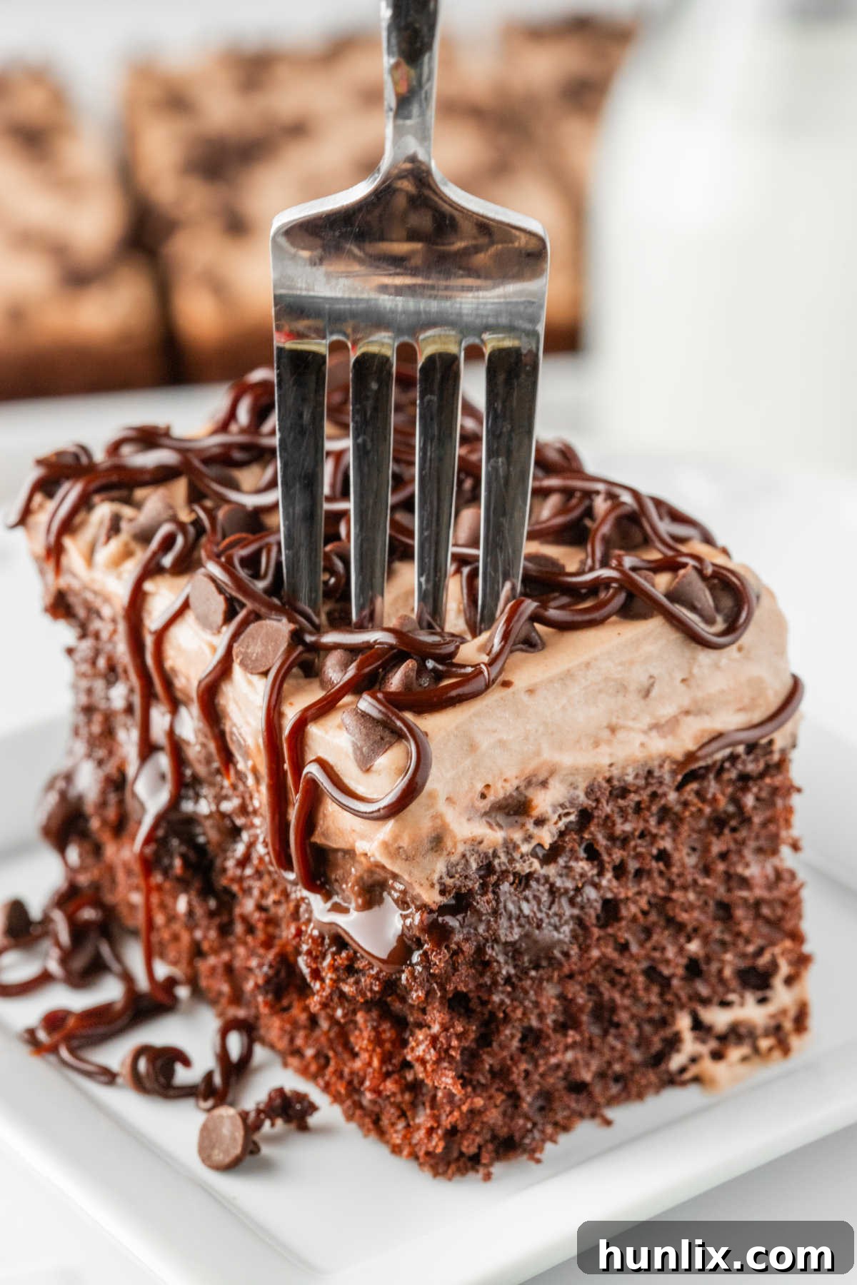 Decadent Triple Chocolate Poke Cake 10 A piece of cake on a plate with a fork in it.
