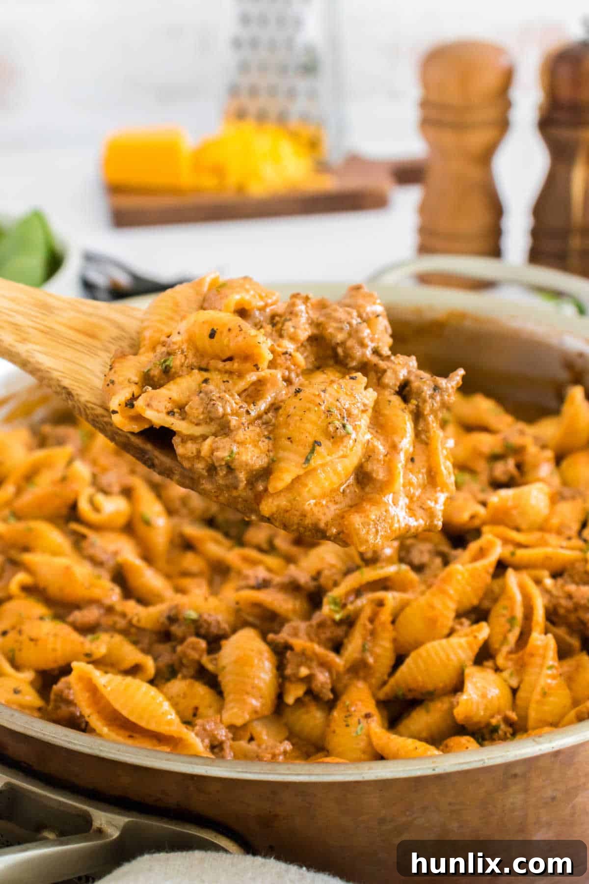 A serving spoon lifting creamy beef and shells from a large bowl, showcasing the rich sauce and tender pasta.