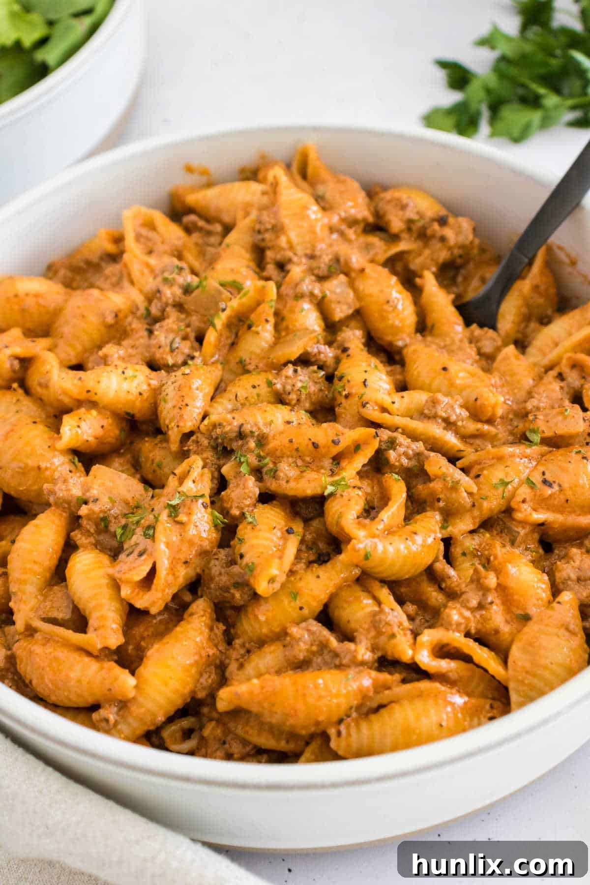 A beautifully plated bowl of creamy beef and shells, garnished with fresh herbs.