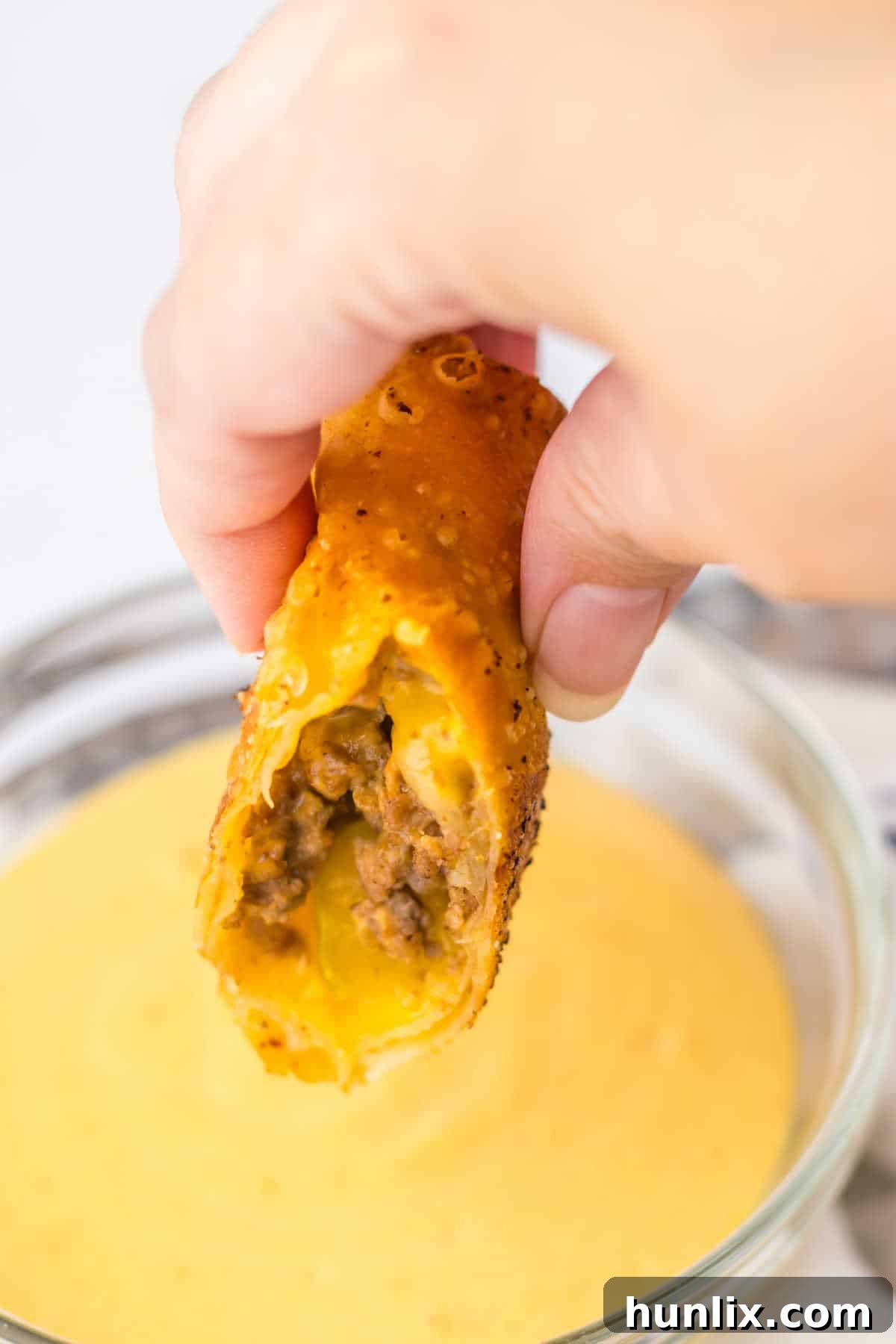 A hand holding a cut Big Mac egg roll over dipping sauce.