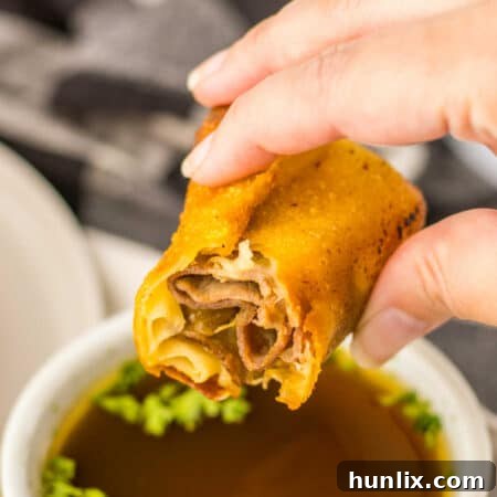 Crispy French Dip Dippers 9 A French dip egg roll cut in half, expertly dipped into a small white bowl of rich au jus sauce.
