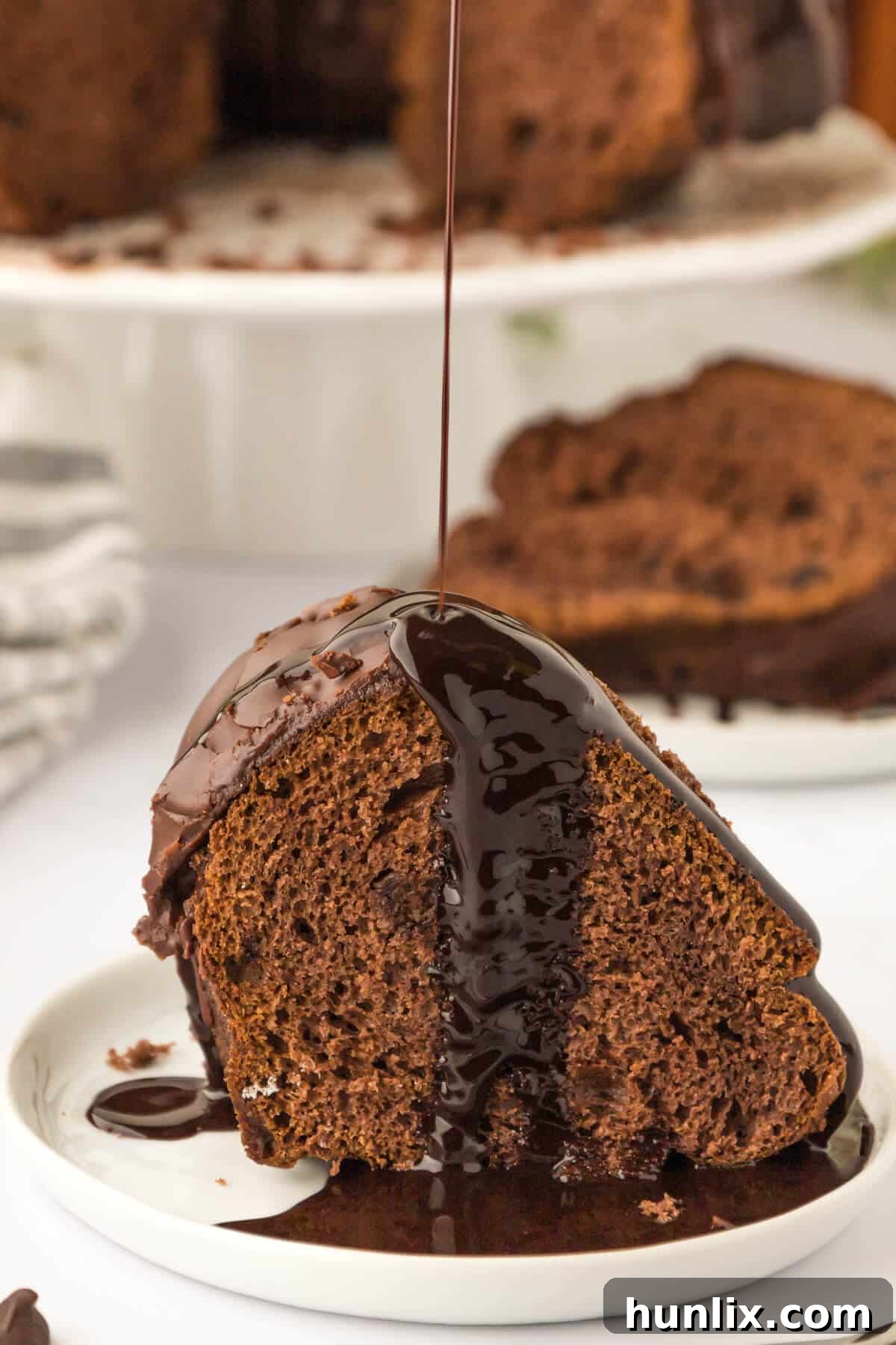 A piece of cake on a plate with chocolate sauce being drizzled on.