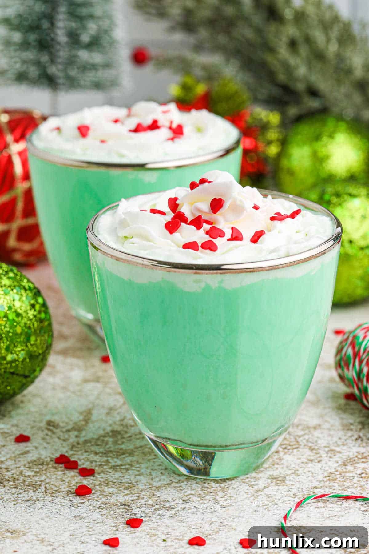 The Grinch Mint Cocktail artfully presented in a stylish glass mug, garnished with whipped cream and red heart sprinkles, set against a festive backdrop.