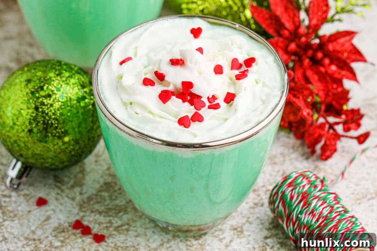 A beautifully presented non-alcoholic Grinch Mint Mocktail in a glass mug, topped with whipped cream and red sprinkles.