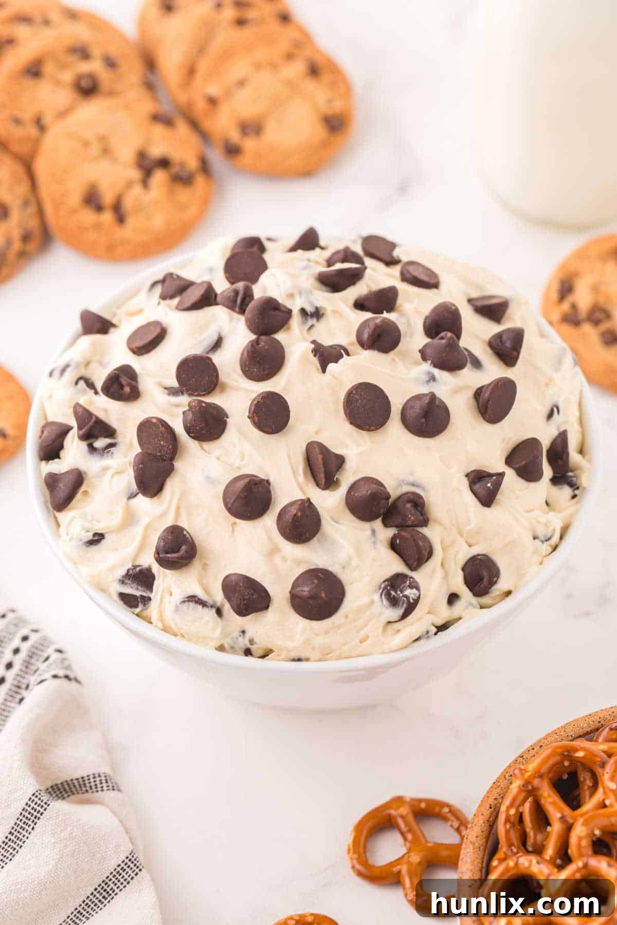 No-Bake Cookie Dough Dip 6 A large bowl of creamy cookie dough dip adorned with chocolate chips, surrounded by various dippers on a platter.