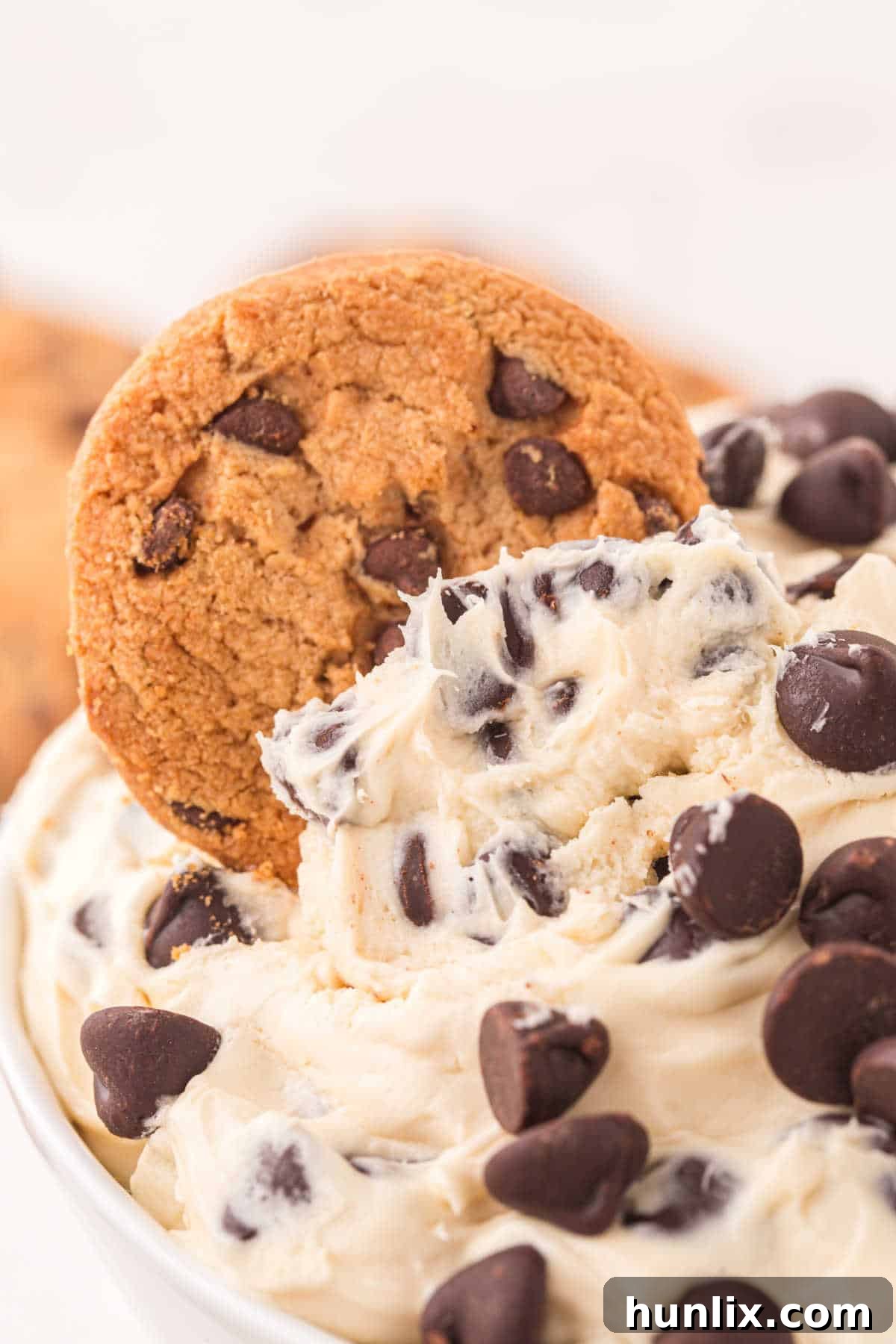 No-Bake Cookie Dough Dip 7 A close-up of a chocolate chip cookie being dipped into a bowl of rich cookie dough dip.