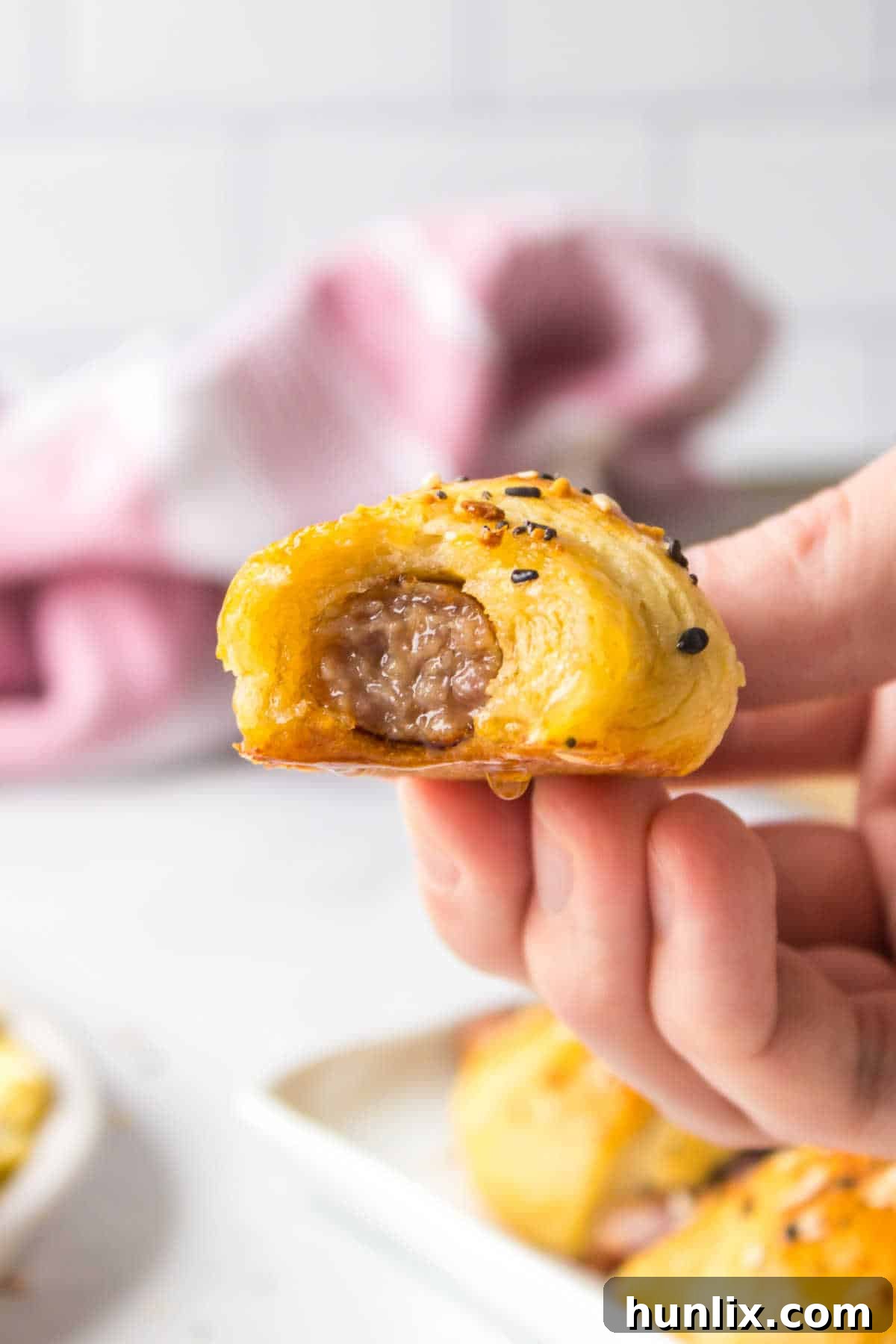 A hand holding a perfectly baked breakfast pig in a blanket, ready to eat.