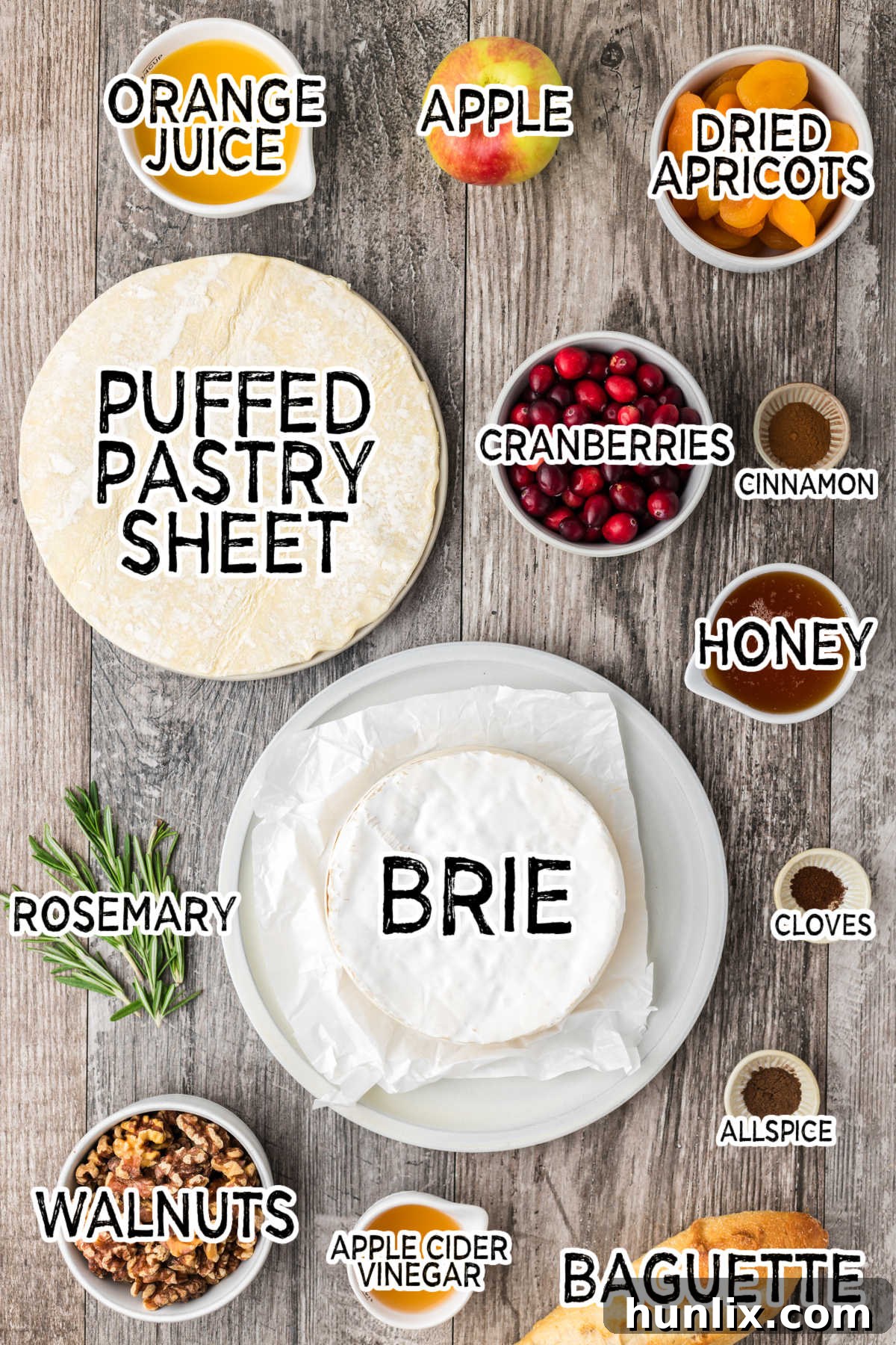 Assortment of fresh ingredients for baked brie and cranberry chutney laid out on a rustic wooden background, including cranberries, apples, walnuts, honey, spices, and a wheel of brie.