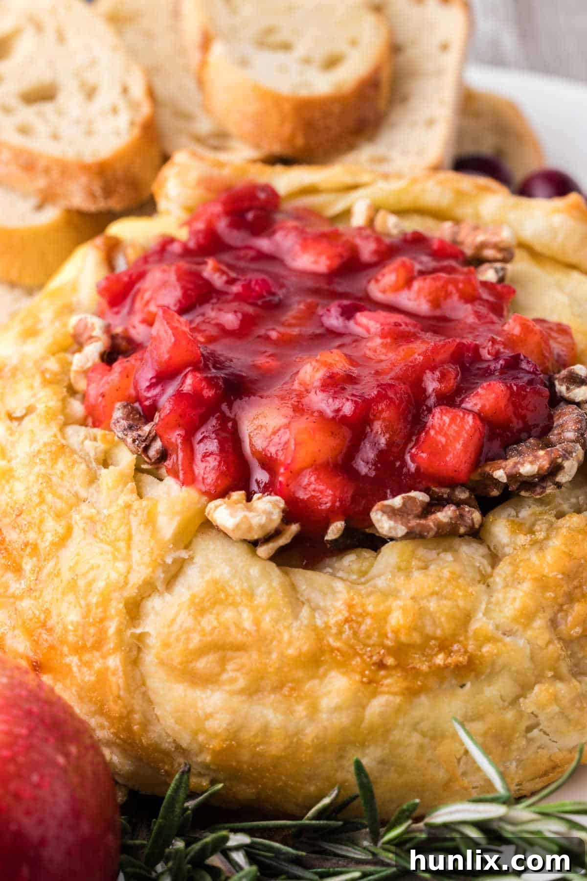 A beautifully presented baked brie with cranberry chutney, walnuts, and rosemary on a plate, surrounded by fresh grapes and apple slices, ready to be served.