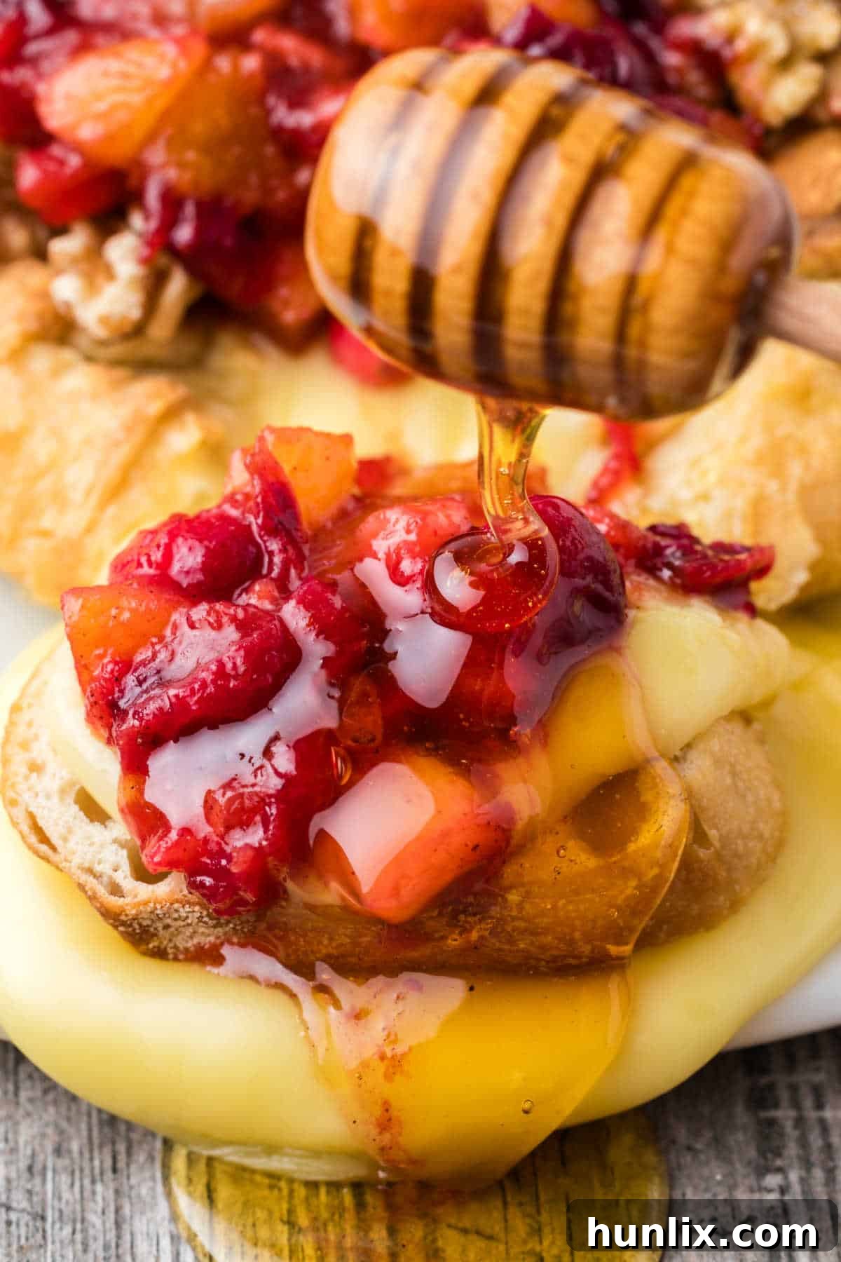 A close-up of a baked brie with cranberry chutney, showing honey being drizzled over the top, emphasizing its luxurious and sweet appeal.