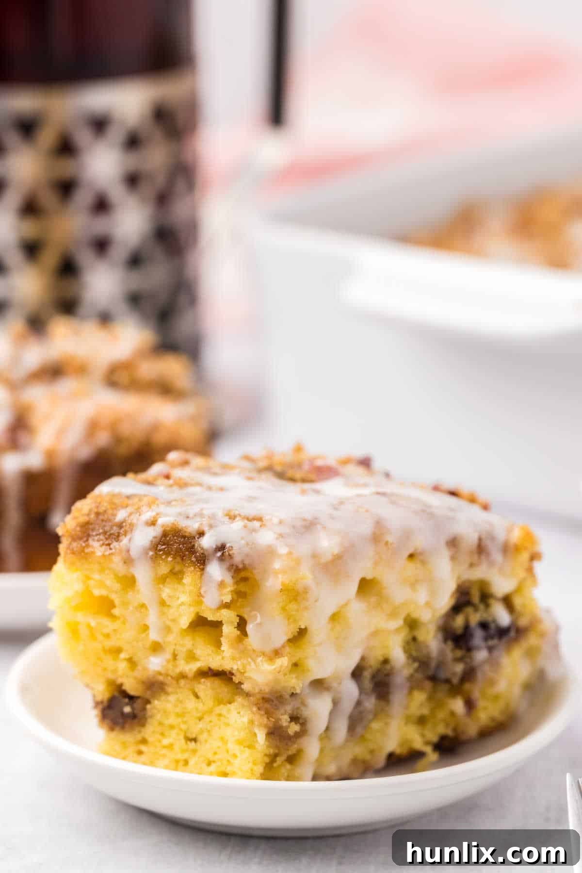 A slice of coffee cake with streusel topping and glaze, served on a white plate.