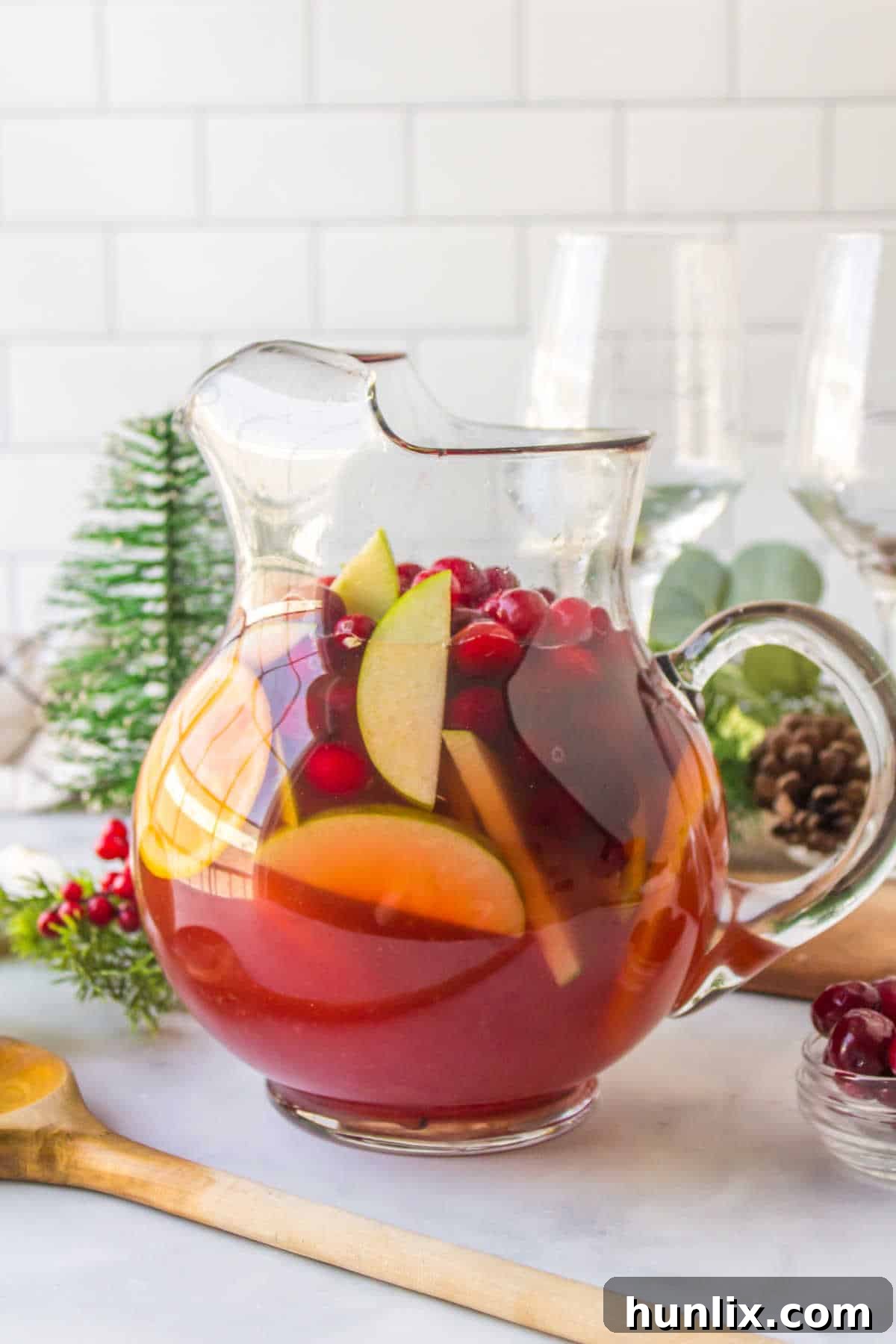 Holiday sangria in a pitcher, garnished with fresh fruit and cinnamon sticks.