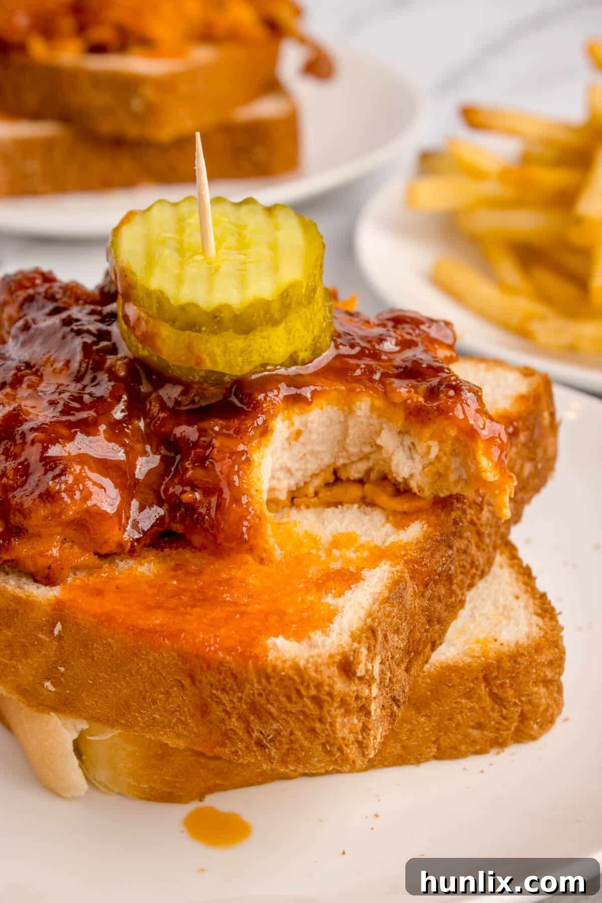 Crispy Air-Fried Nashville Heat 9 A plate of Air Fryer Nashville Hot Chicken with a piece having a bite taken out, showing its juicy interior.