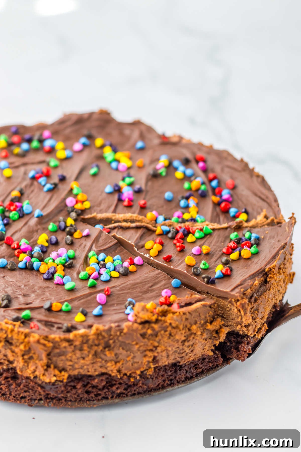 Brownie Nebula Cheesecake 2 A perfectly sliced Cosmic Brownie Cheesecake revealing its layers: fudgy brownie crust, creamy chocolate cheesecake, and glossy ganache topped with rainbow sprinkles.