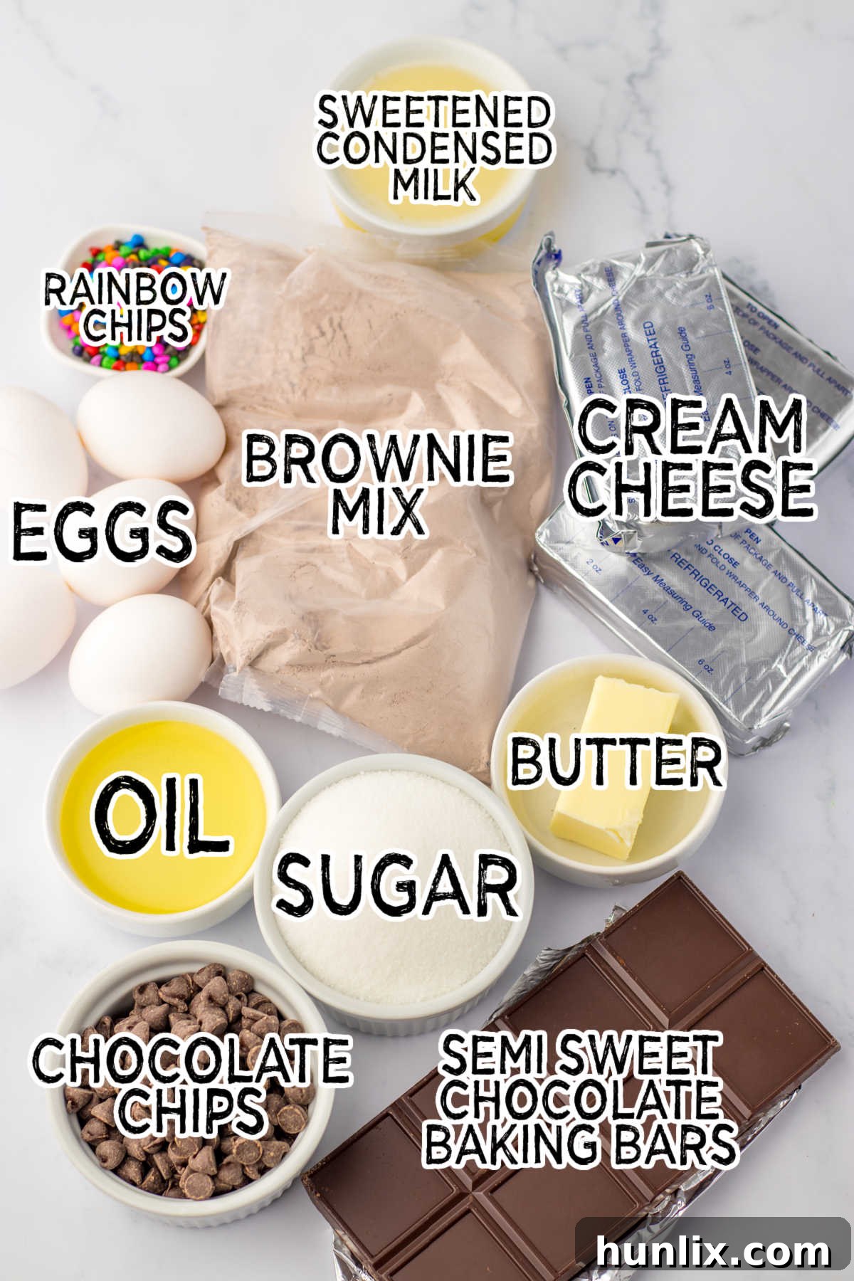 Brownie Nebula Cheesecake 3 A flat lay photograph showcasing all the ingredients required to make a Cosmic Brownie Cheesecake, including brownie mix, cream cheese, sugar, chocolate bars, eggs, butter, condensed milk, chocolate chips, and rainbow sprinkles.