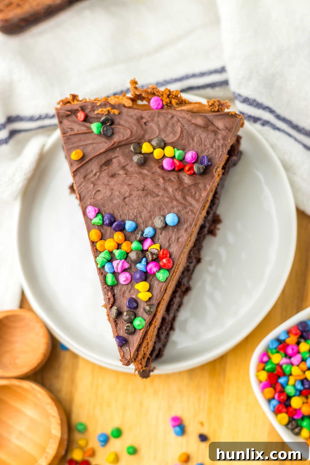 Brownie Nebula Cheesecake 9 A close-up shot of a whole Cosmic Brownie Cheesecake with a slice removed, displaying its luscious layers of brownie, chocolate cheesecake, and ganache with colorful sprinkles.