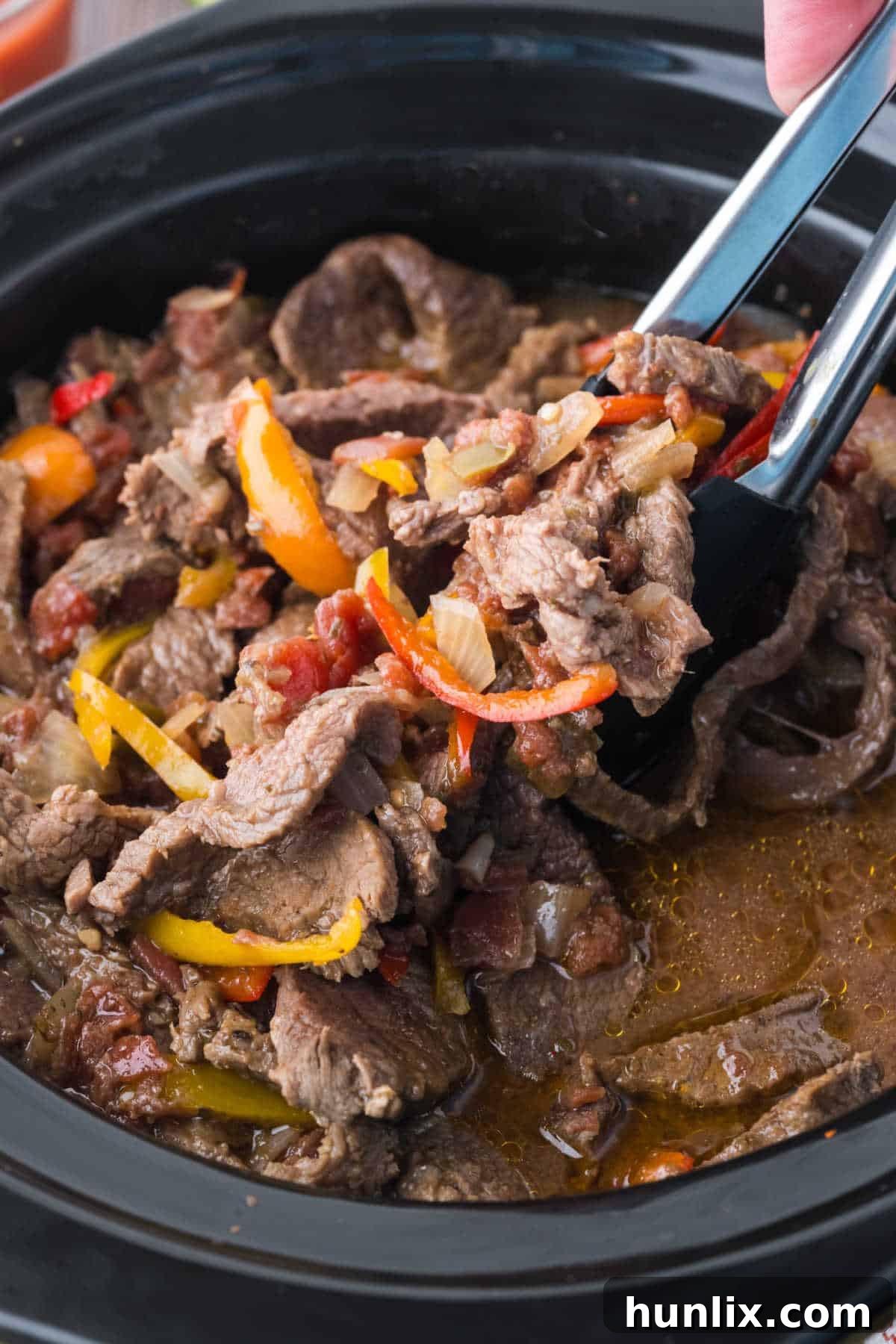 Tongs lifting tender steak fajitas from a slow cooker, ready to be served.