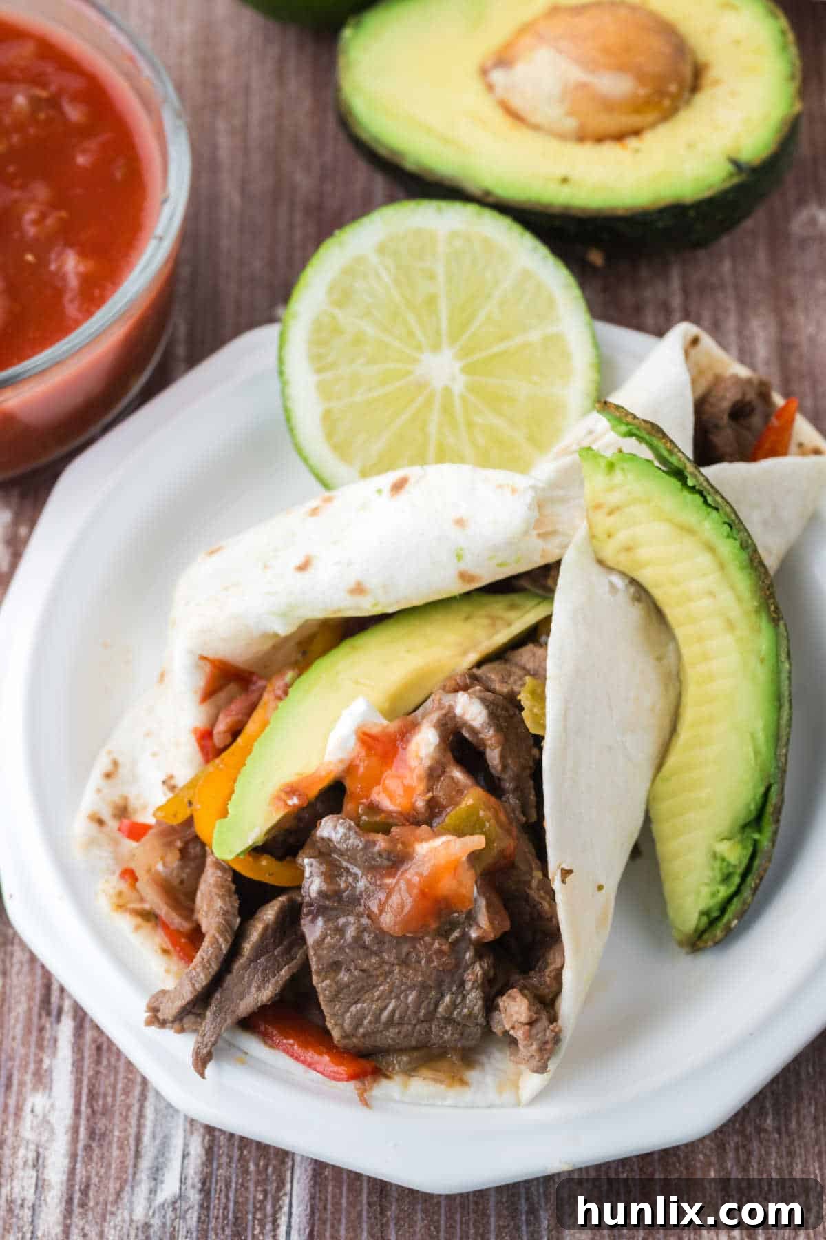 Steak fajitas served on a plate with fresh avocado slices and lime wedges, showcasing a vibrant and appealing meal.