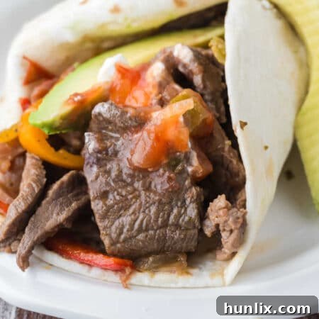 Slow cooker steak fajitas on a plate with fresh garnishes.