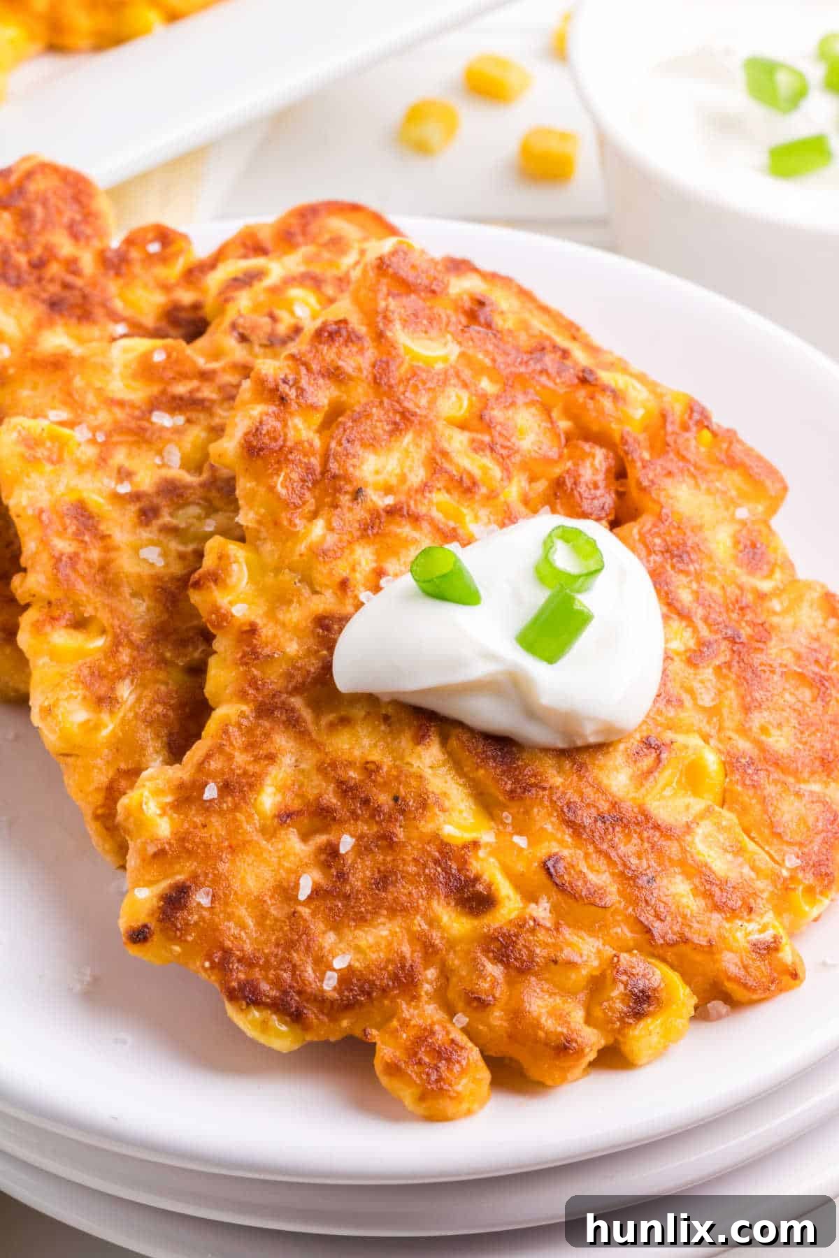 Golden Corn Bites 2 A vibrant plate of golden-brown corn fritters, garnished with fresh herbs, invitingly stacked and ready to be enjoyed.