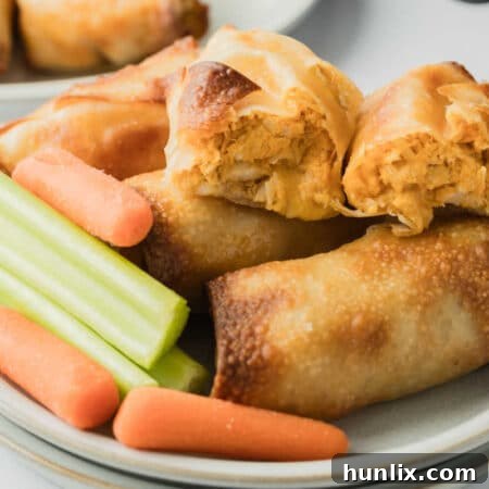 A plate of crispy Air Fryer Buffalo Chicken Egg Rolls with carrot and celery sticks.