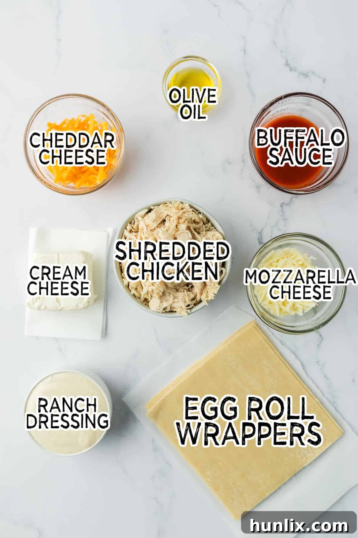 A flat lay image displaying all the raw ingredients for Buffalo Chicken Egg Rolls laid out on a marble countertop.