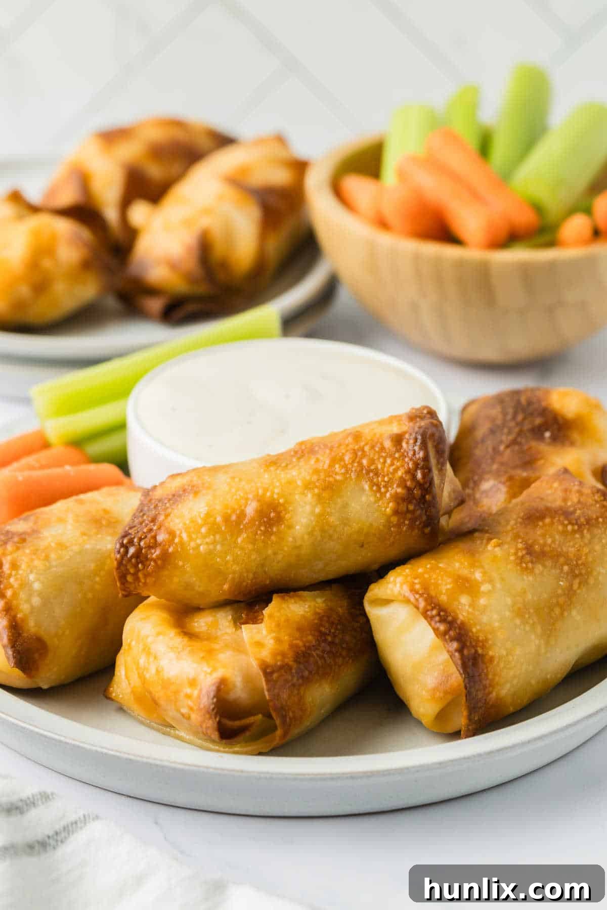 A plate of freshly air-fried buffalo chicken egg rolls, accompanied by a small bowl of ranch dressing for dipping.