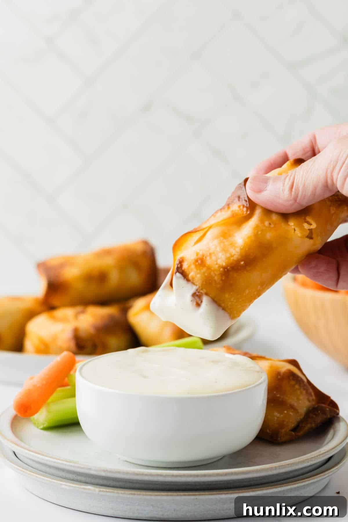 A hand dipping a crispy buffalo chicken egg roll into a small bowl of creamy ranch dressing.