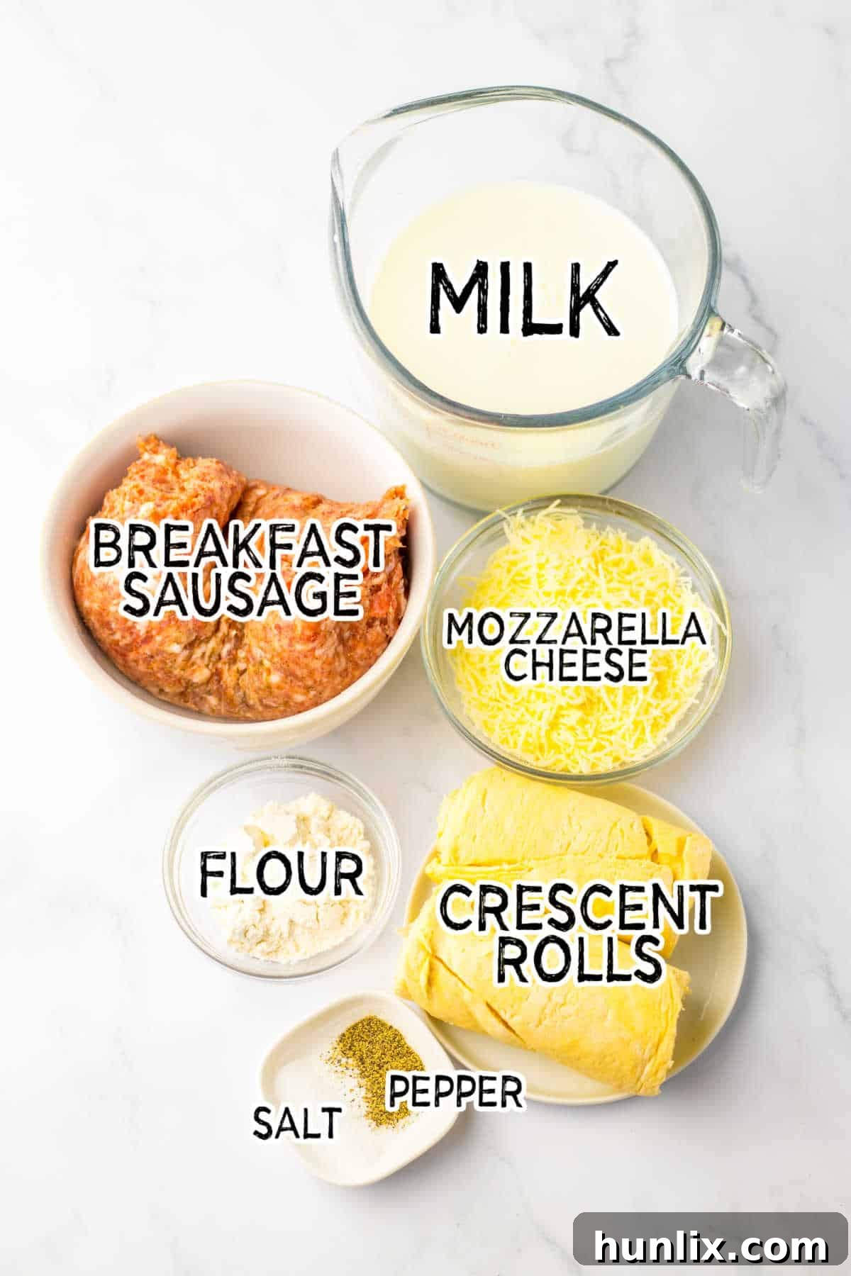 All the fresh ingredients for School Breakfast Pizza displayed on a white marble counter, including sausage, flour, milk, cheese, and crescent rolls.